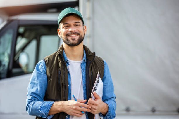 Delivery driver smiling, holding clipboard, standing beside his truck.
