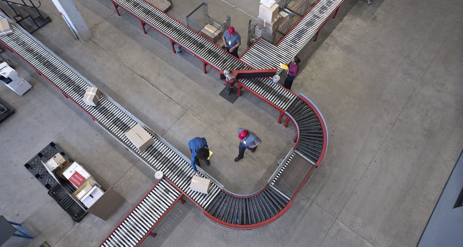 Overhead view of warehouse workers sorting packages on conveyor belts.