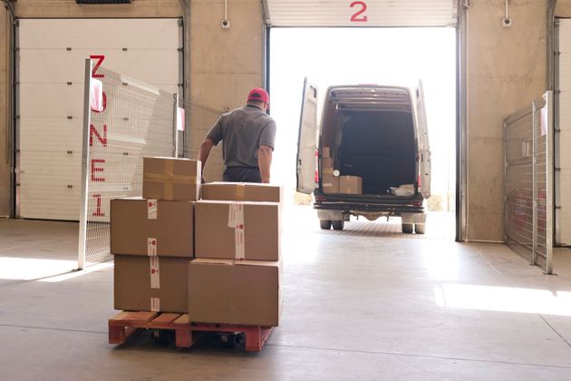 Man loading boxes onto a van inside a warehouse loading bay. Pallet of boxes in foreground.