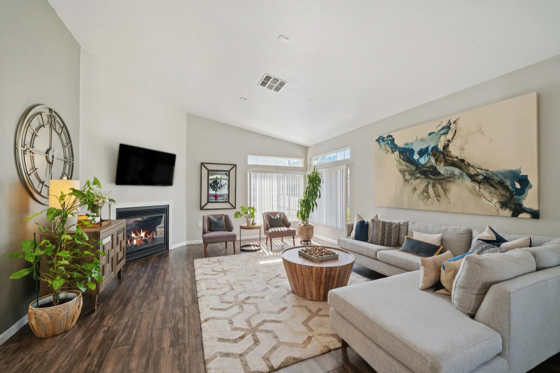 Bright living room with a gray sectional, fireplace, wall art, and large windows.