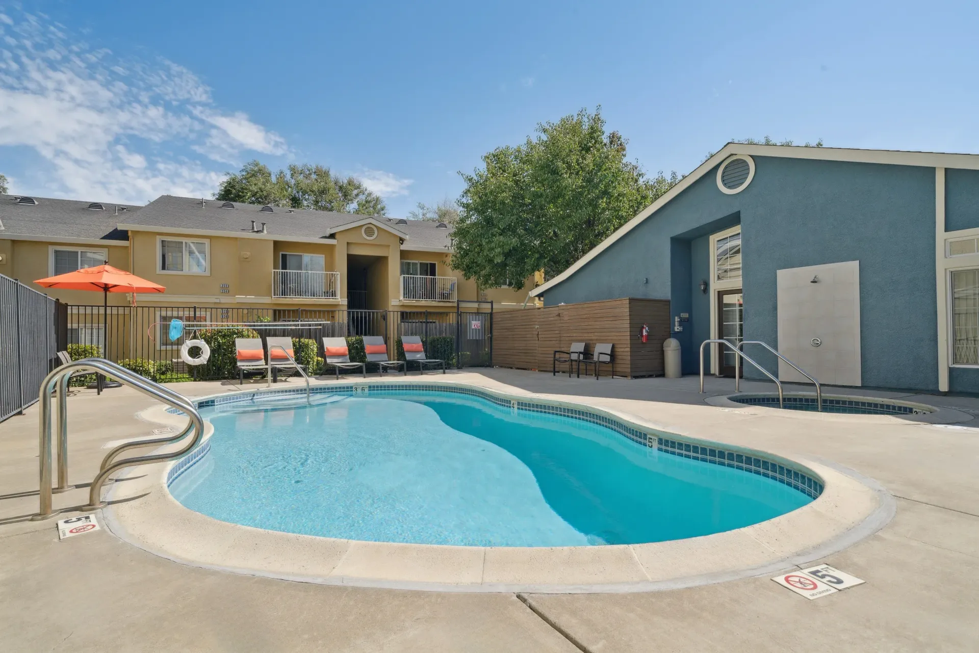 Outdoor apartment pool with lounge chairs and an orange umbrella.
