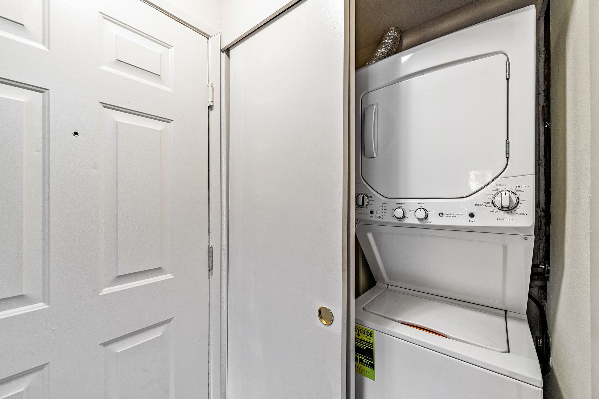 White stacked washer and dryer inside a narrow laundry closet.