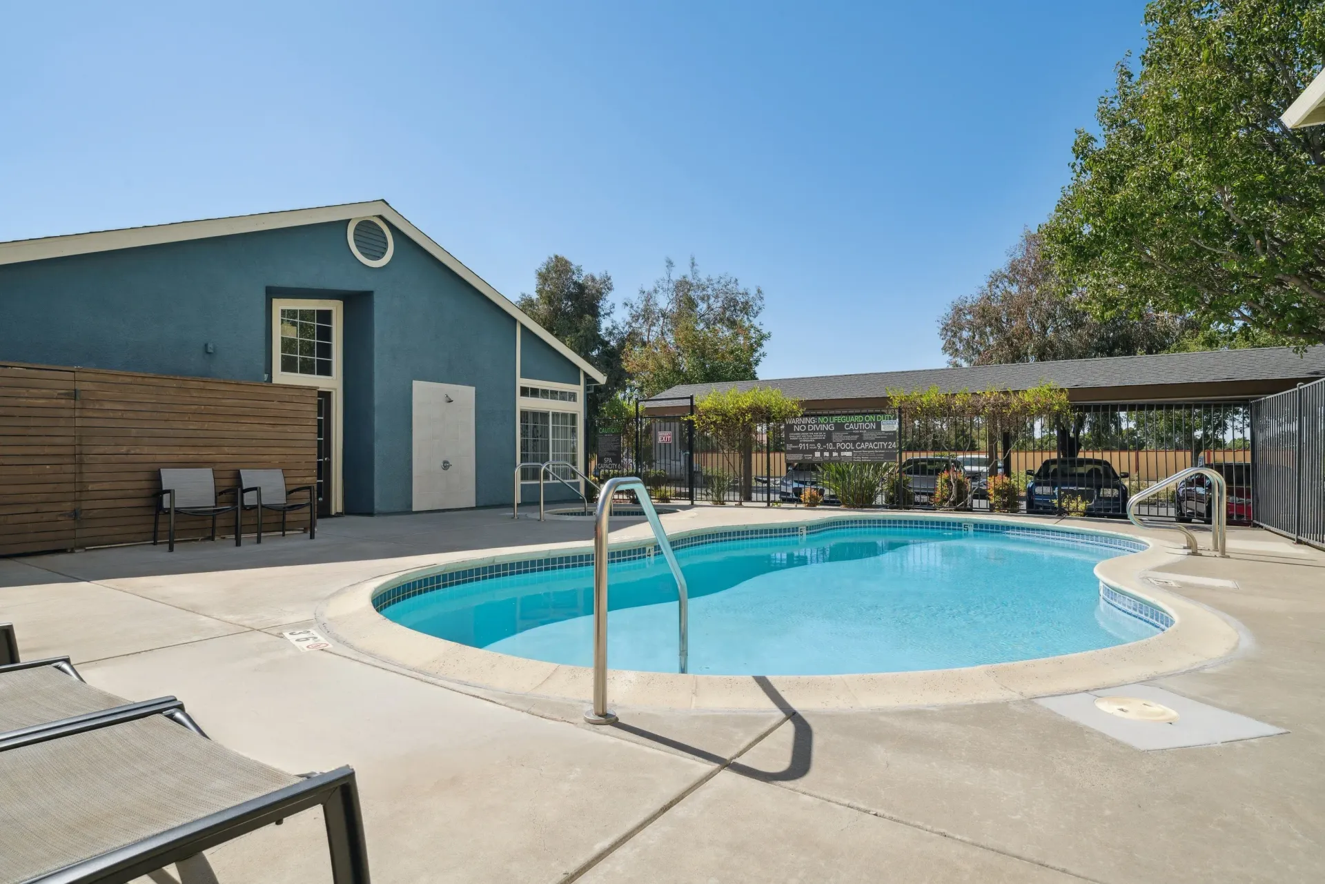 Outdoor pool area at an apartment complex with a blue building and lounge chairs.