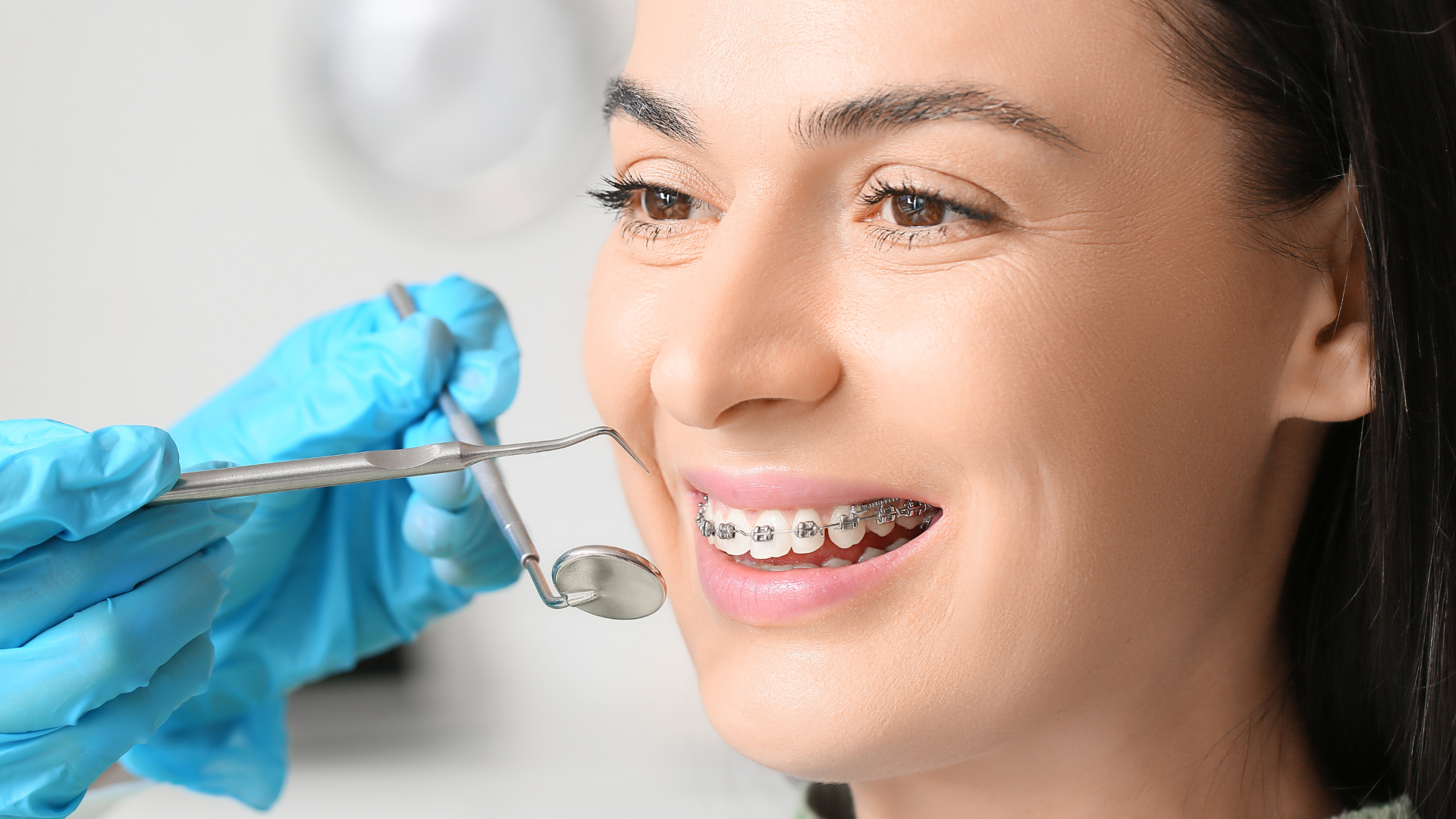 A woman with braces is getting her teeth examined by a dentist.