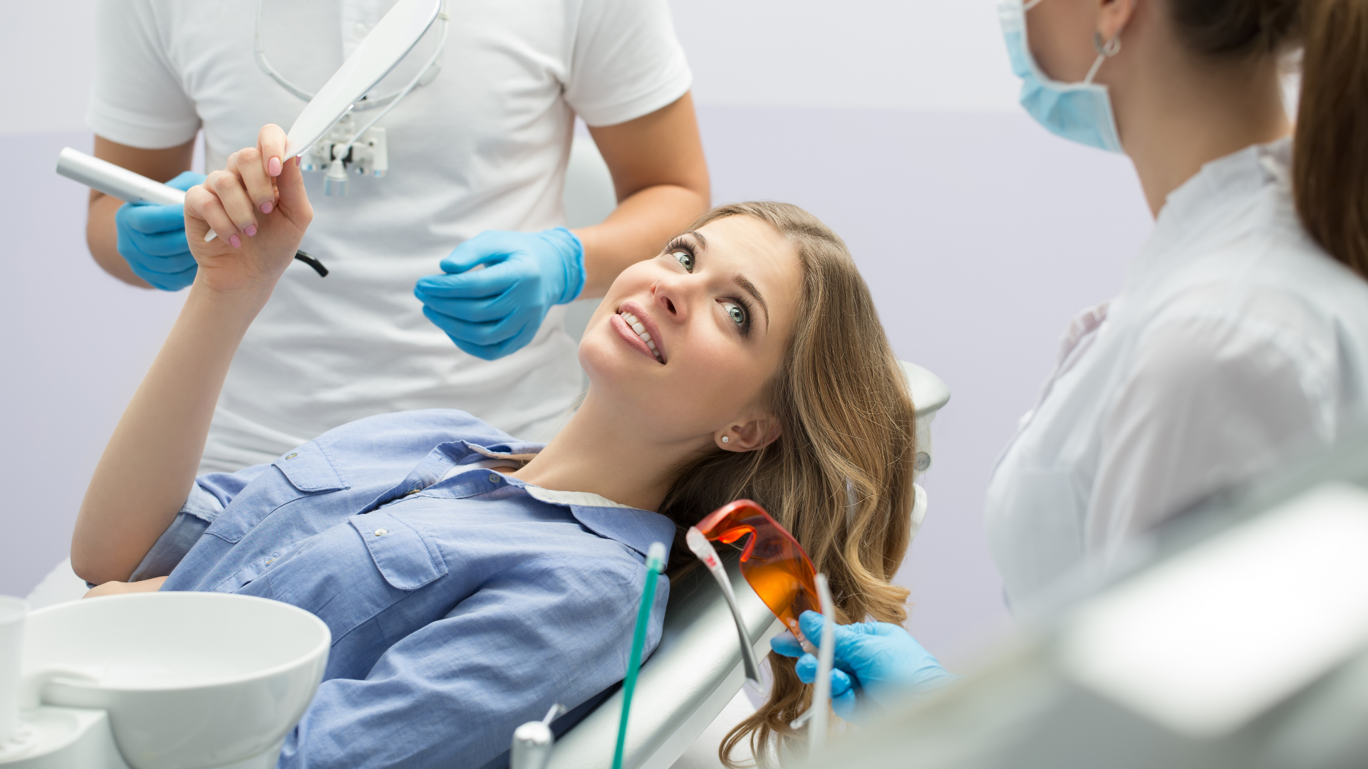 A woman is sitting in a dental chair while a dentist examines her teeth.