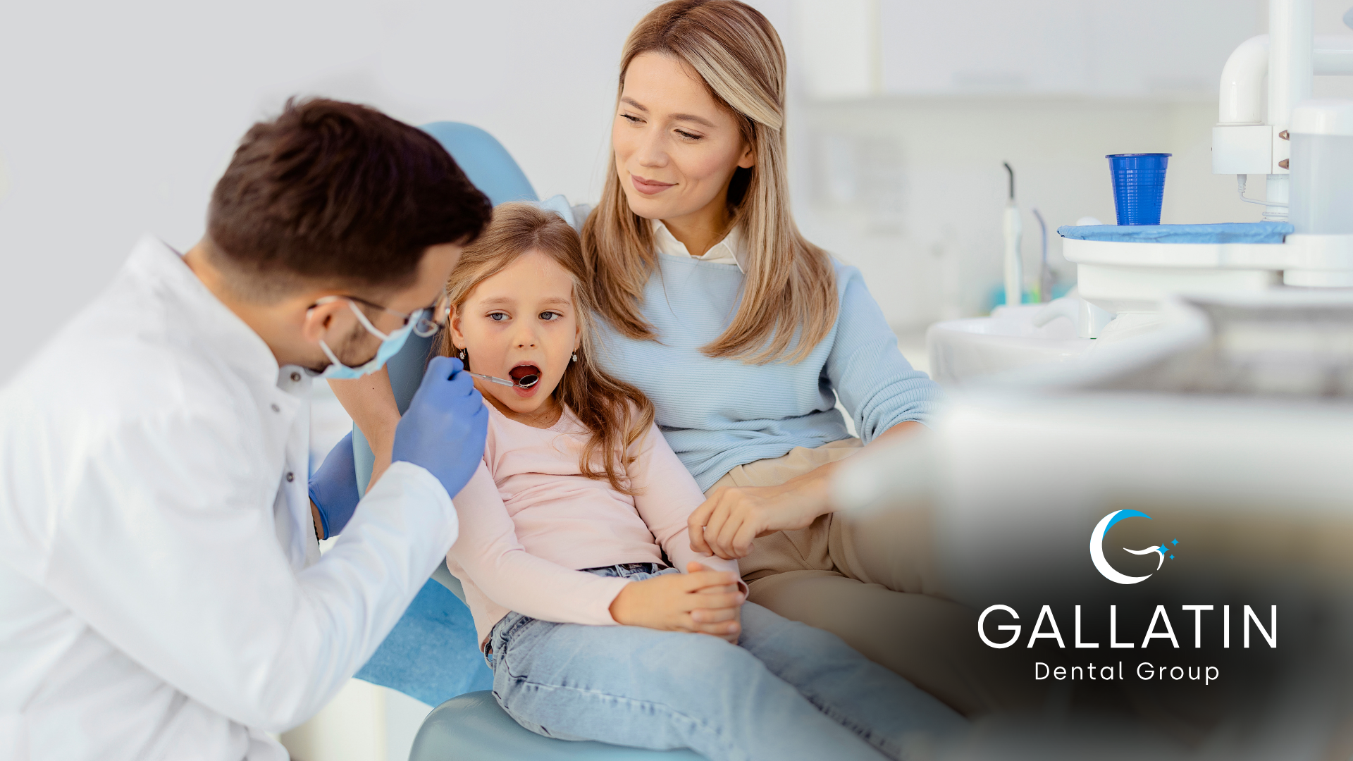 A little girl is sitting in a dental chair while a dentist examines her teeth.