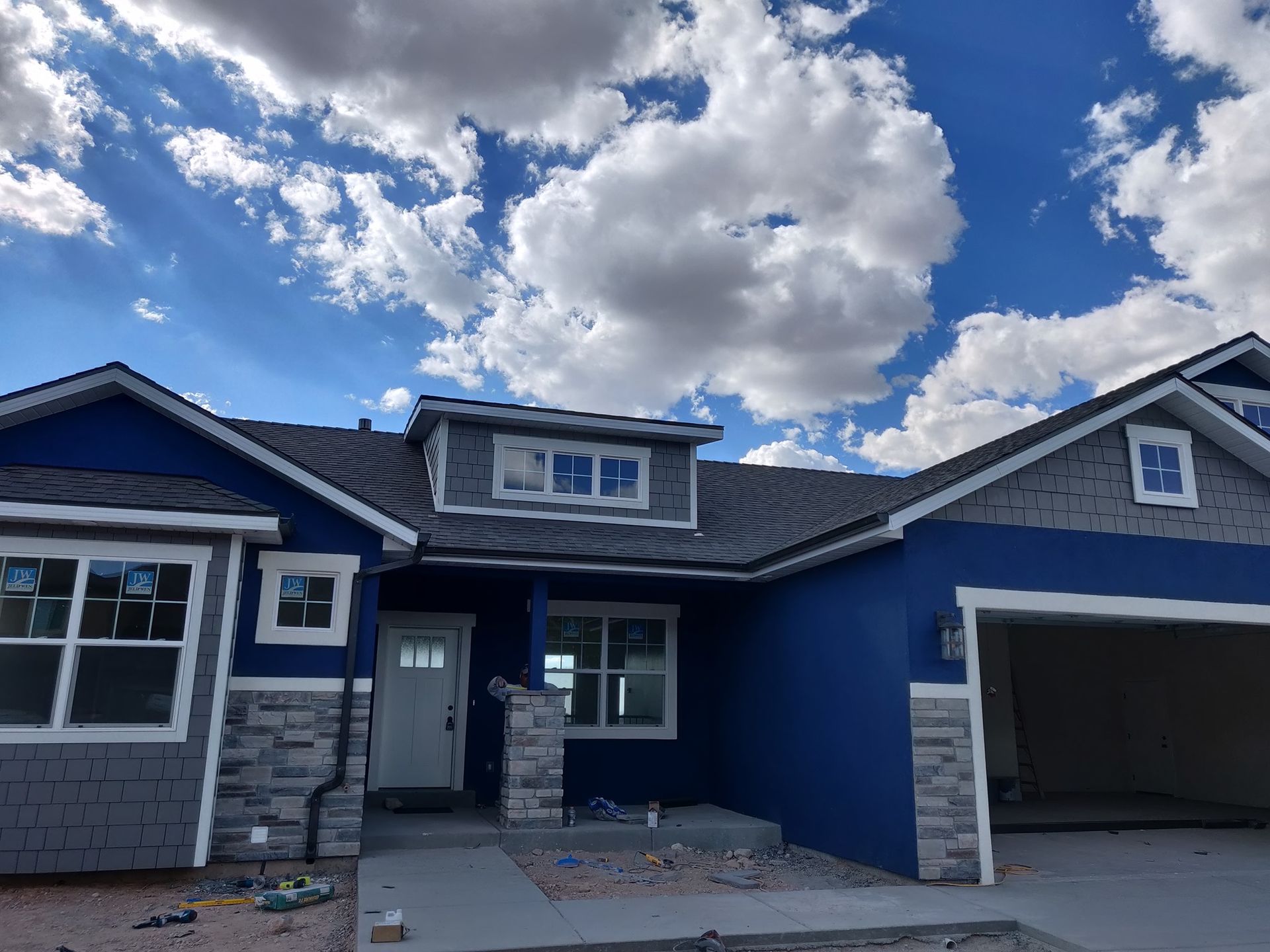 Blue and gray house under a cloudy sky, with a garage and window details.