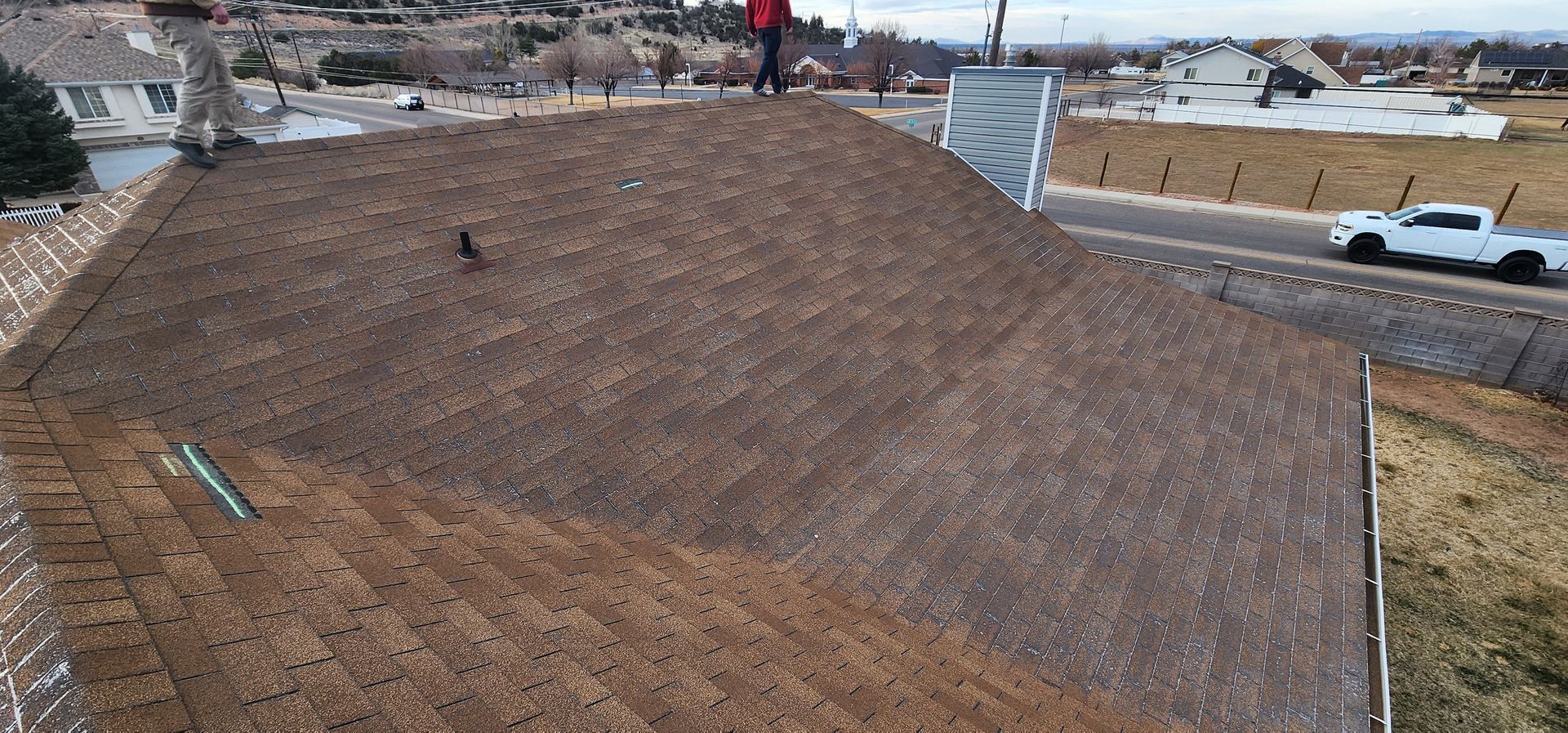 A person standing on a brown roof with a white truck driving on the road nearby.