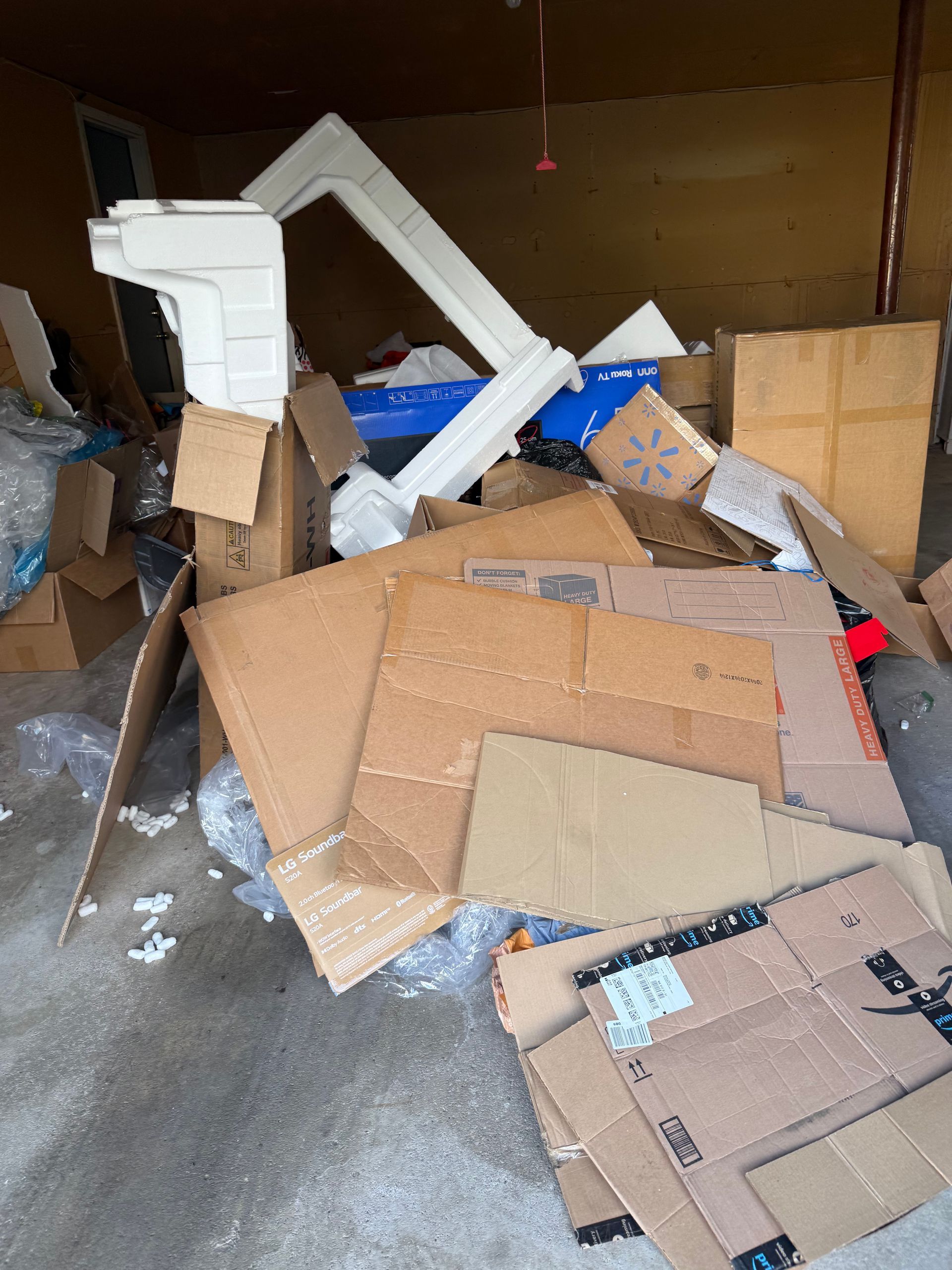 Overflowing cardboard boxes and debris piled in a dim storage room, with a white frame leaning against the wall.