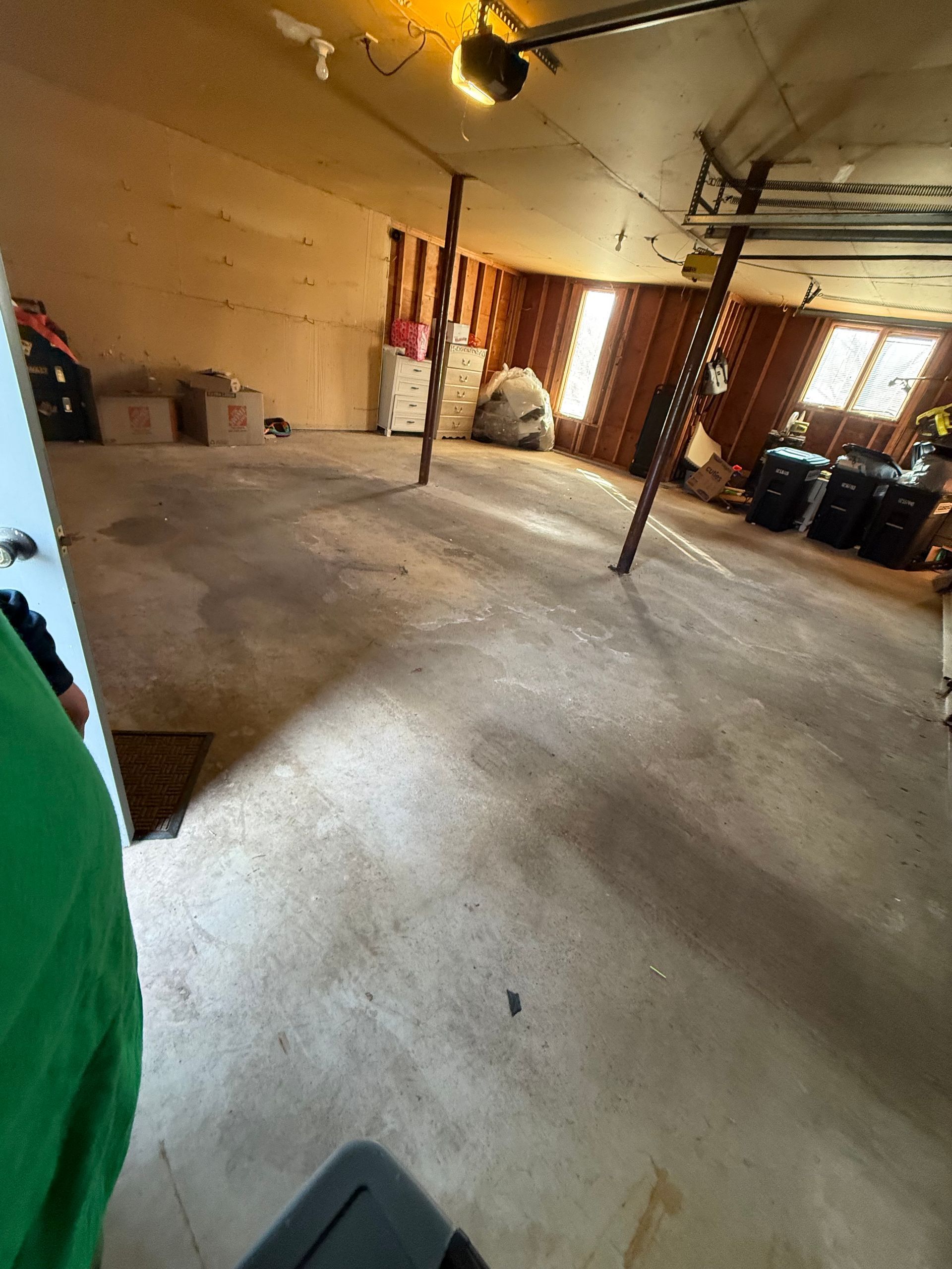 Empty indoor room with bare concrete floor, exposed poles, and warm sunlight from windows.