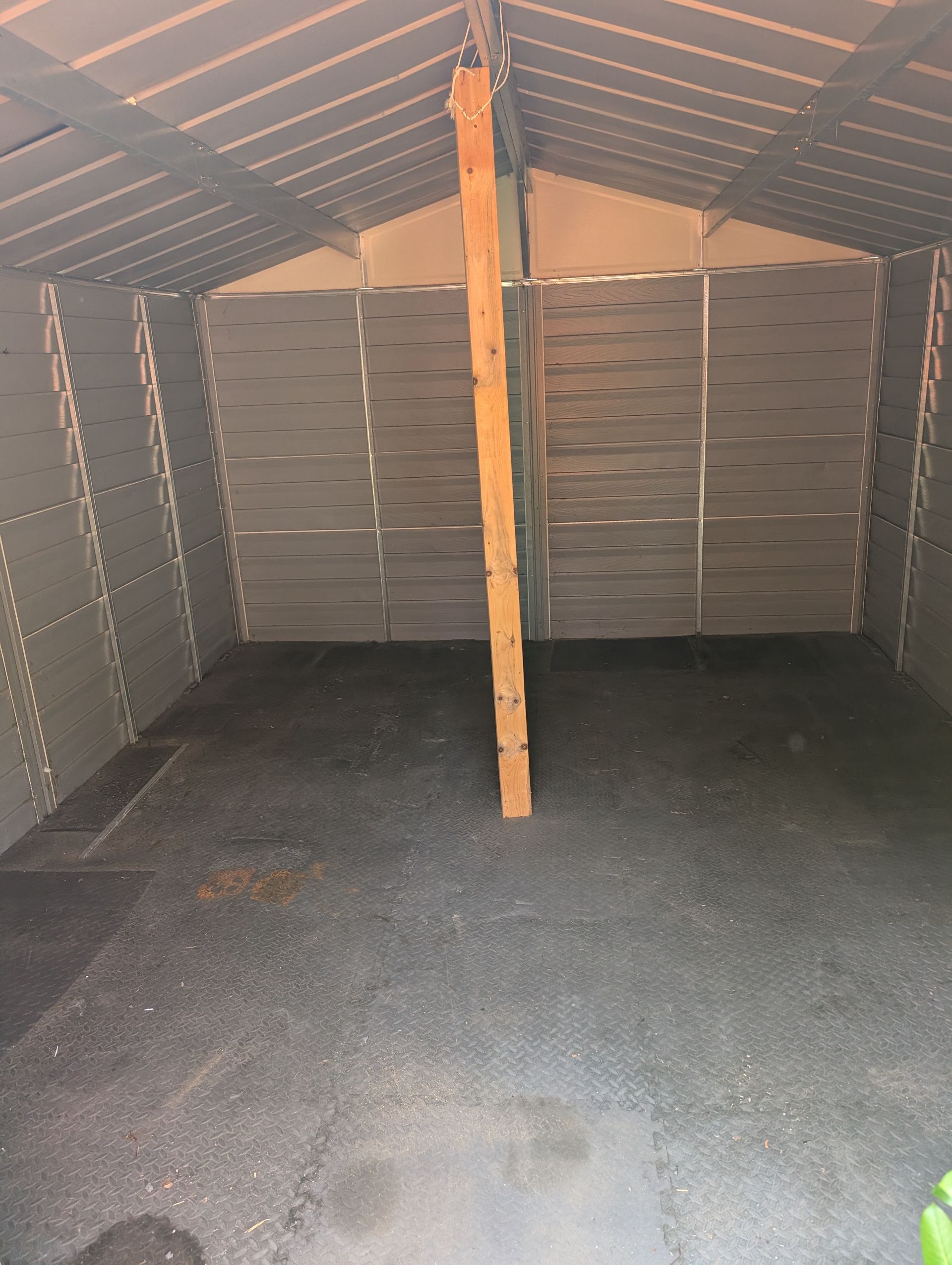 Empty wooden shed interior with slanted roof, central support beam, and dark floor.