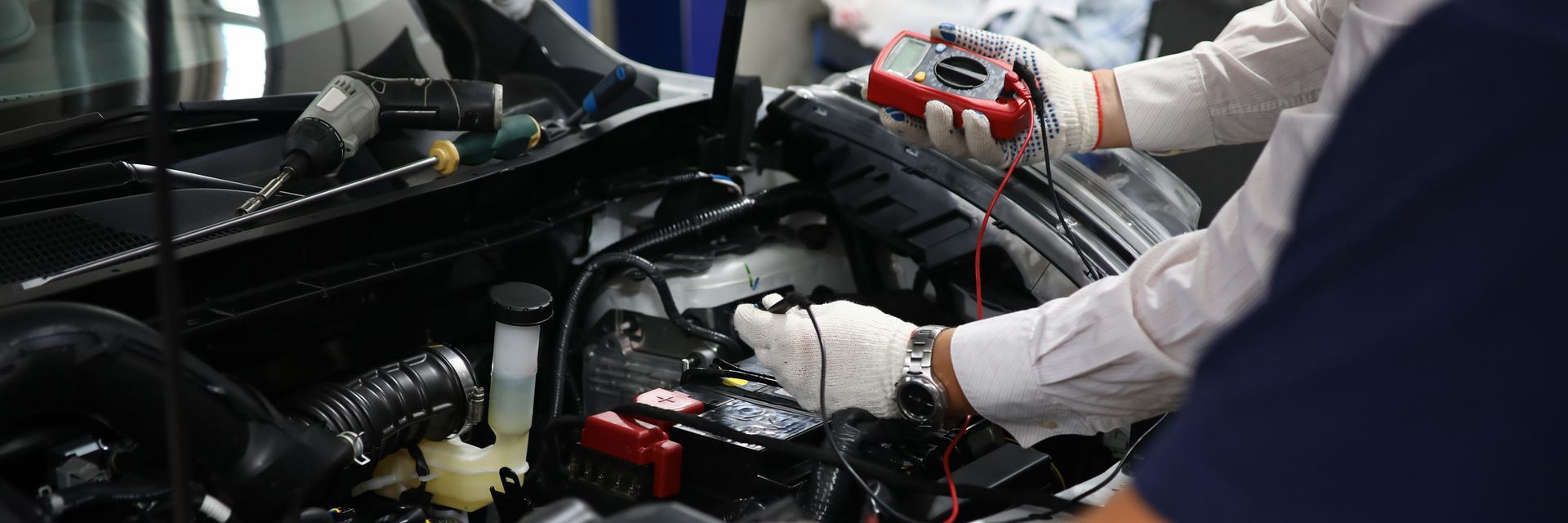 Person in gloves uses a multimeter to inspect a car engine.