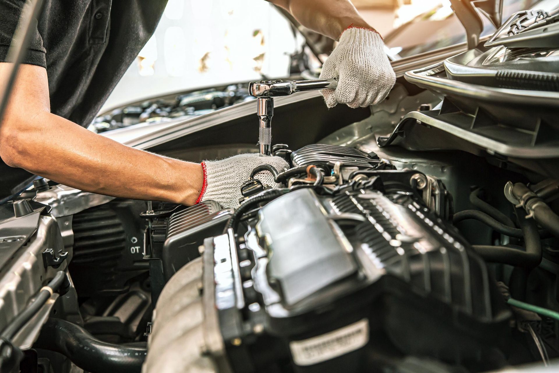 Mechanic working on a car engine, wearing gloves, in a garage.