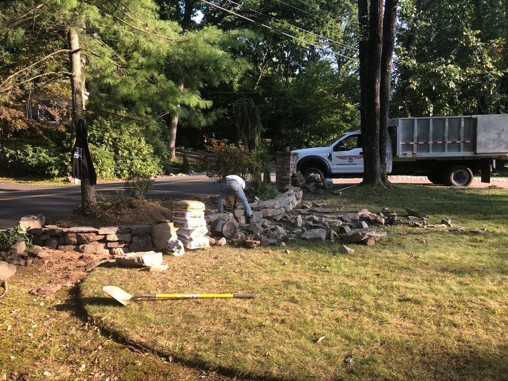 A man is working on a stone wall in a yard next to a truck.