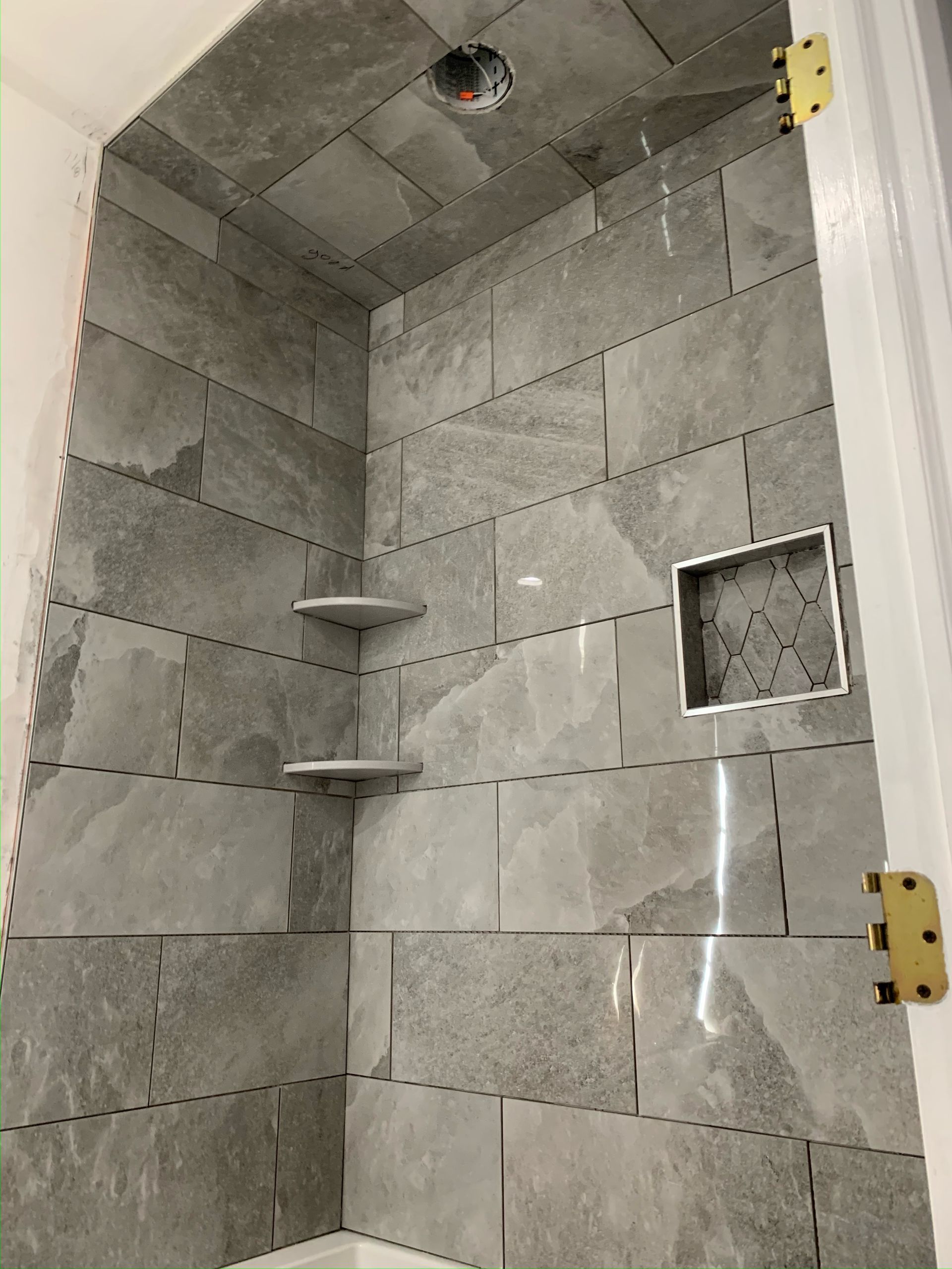 A shower stall with gray tiles and shelves in a bathroom.