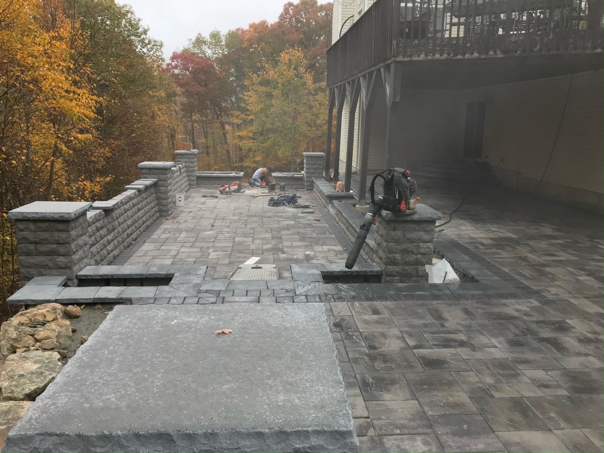 A patio is being built in front of a house with trees in the background.