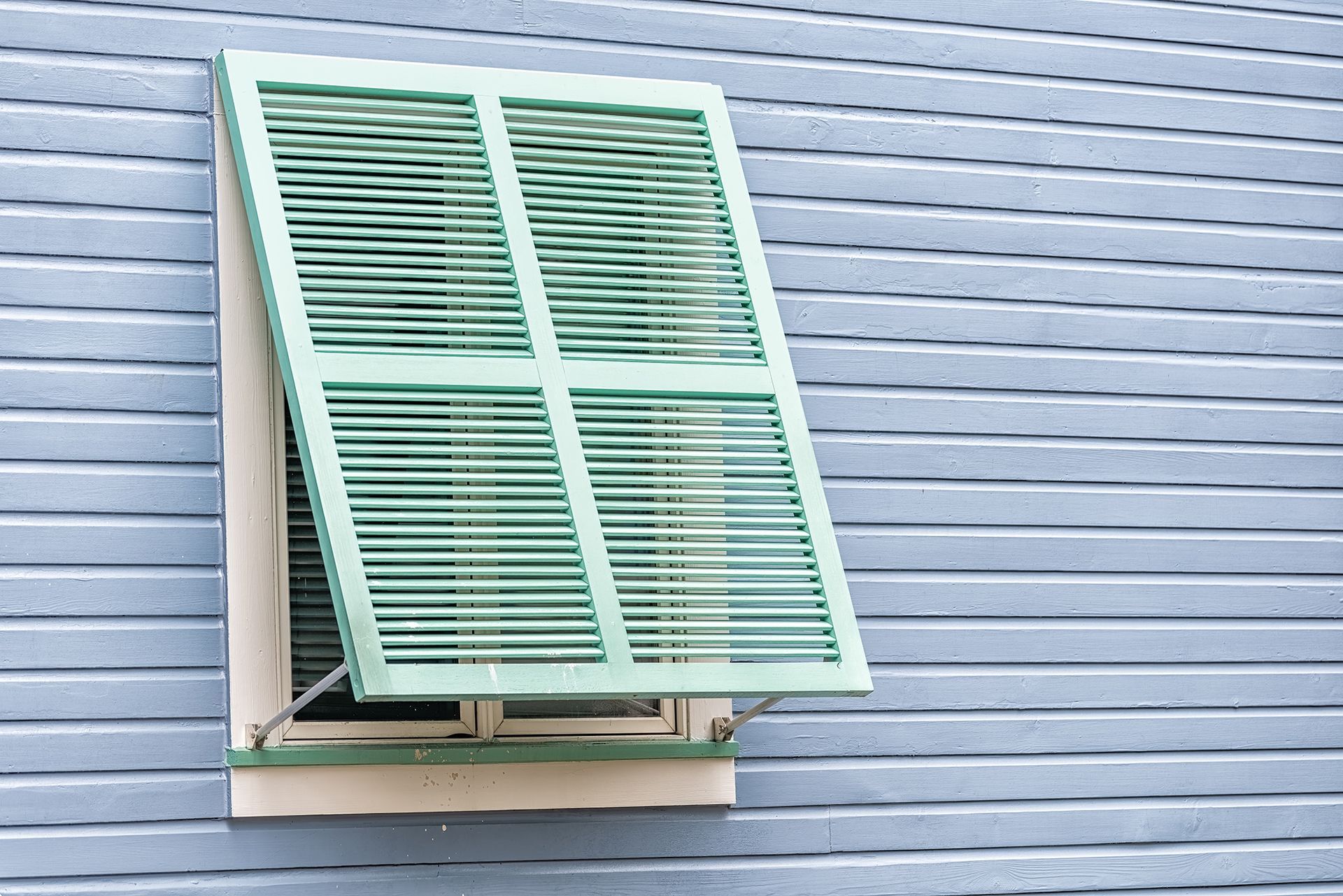 A window with green shutters is open on a blue house.