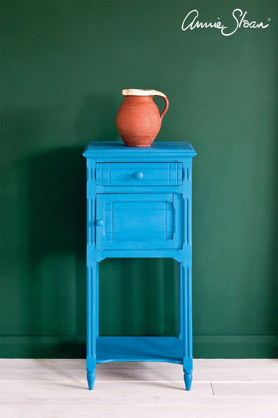 Ein blauer Tisch mit einem Krug darauf vor einer grünen Wand.