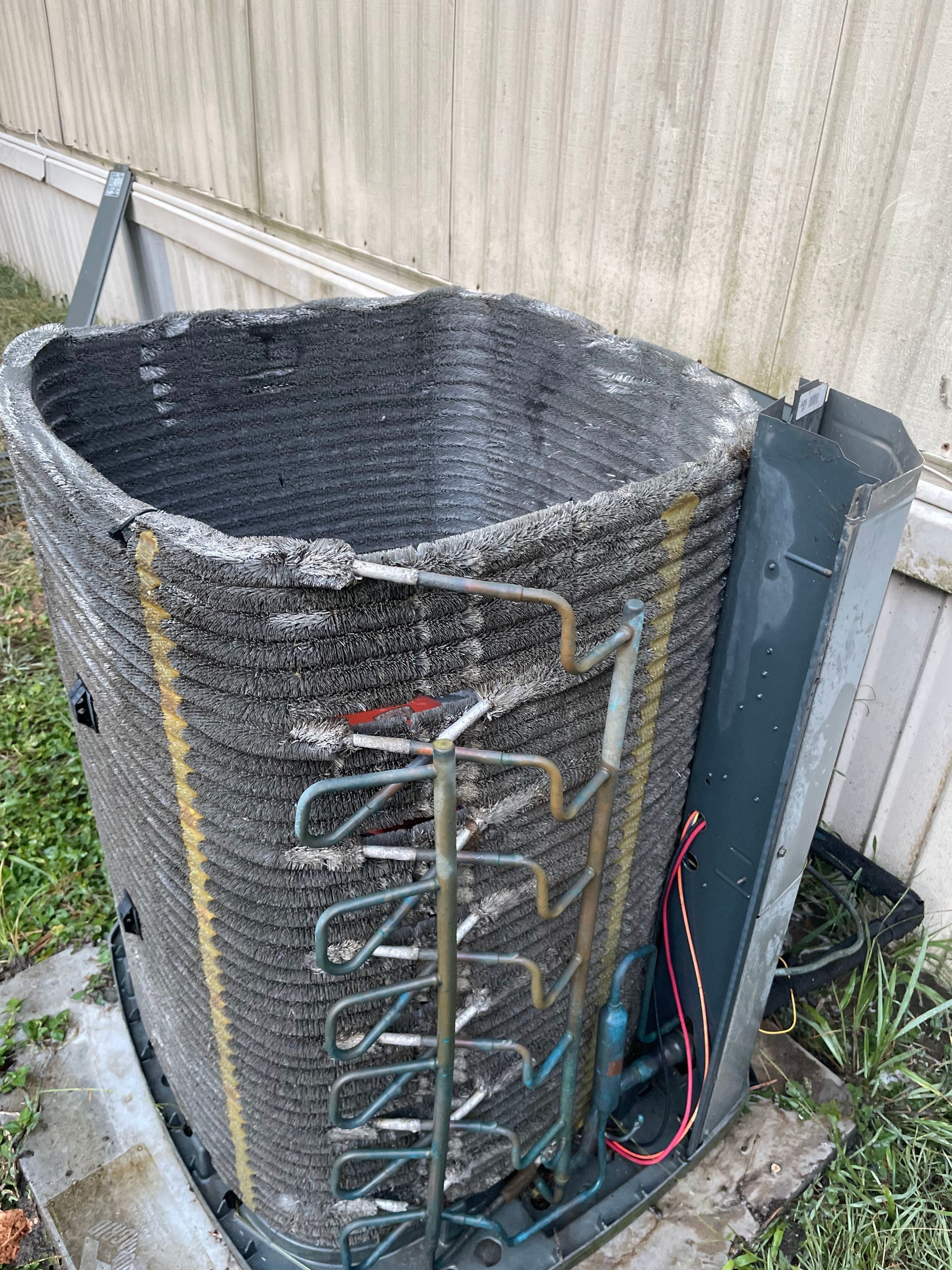Air conditioner unit covered in frost and debris, next to a building.