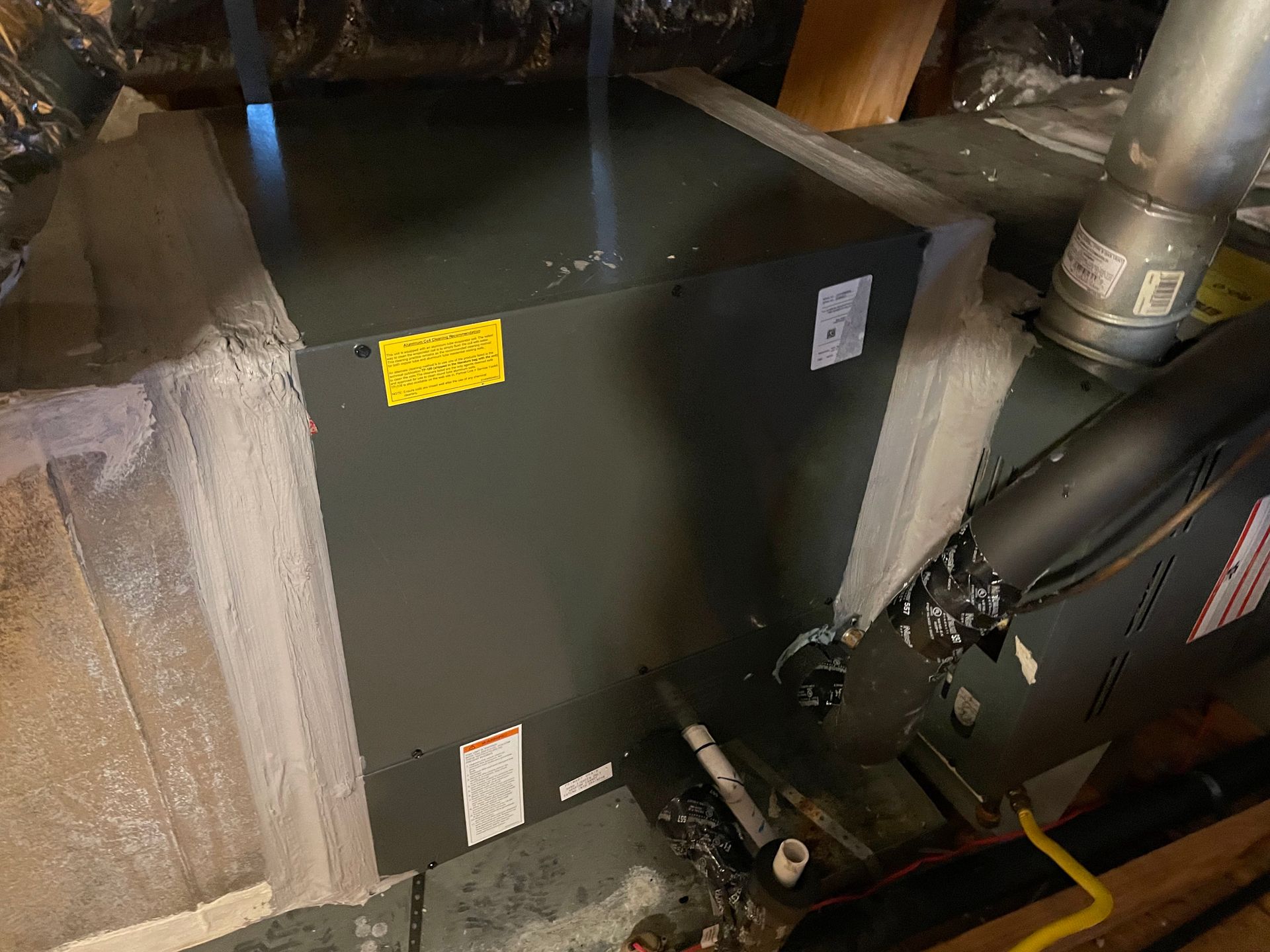 Furnace system in a basement; gray metal unit with ductwork and pipes, insulation visible.