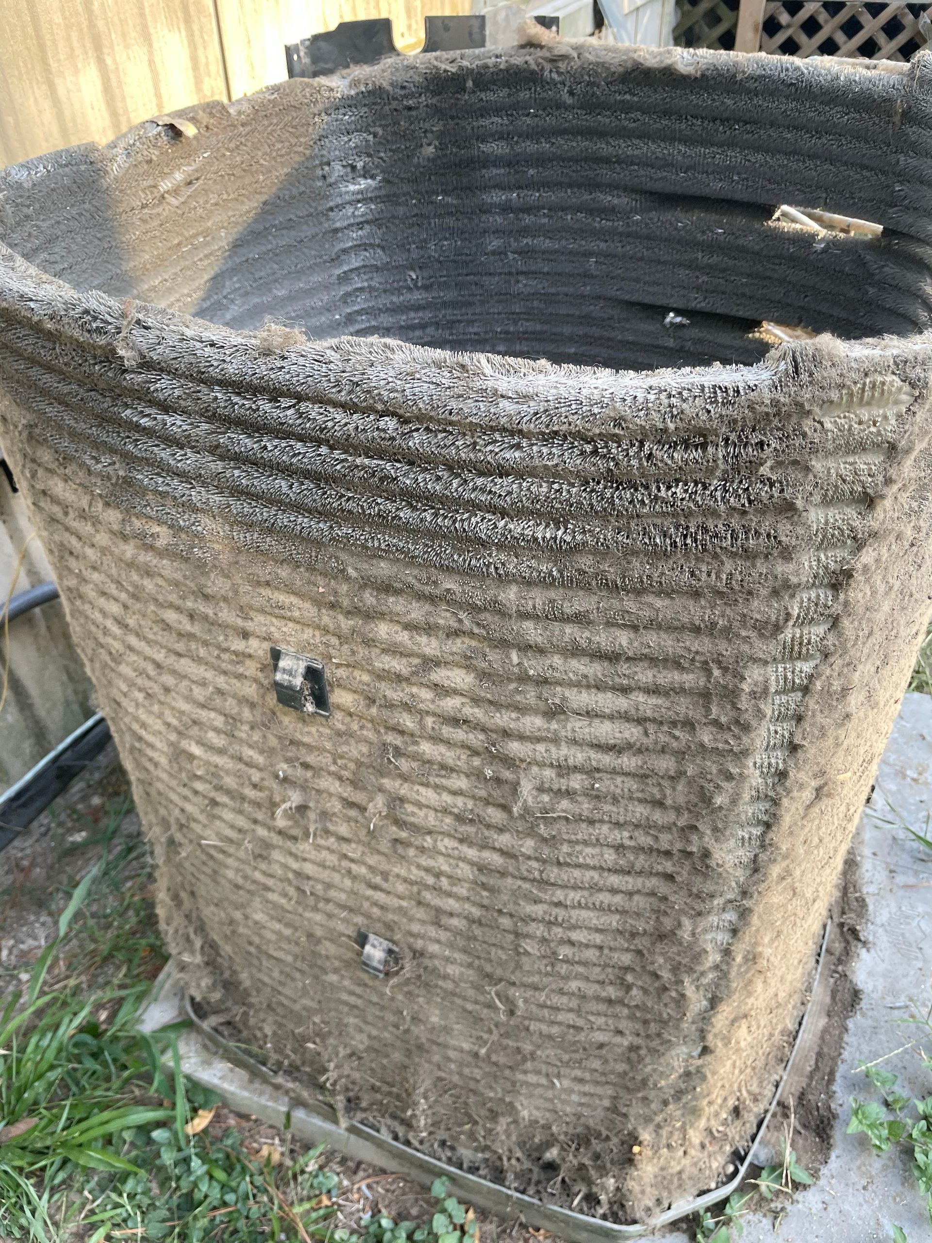 Dirty, cylindrical outdoor air conditioner unit covered in debris.
