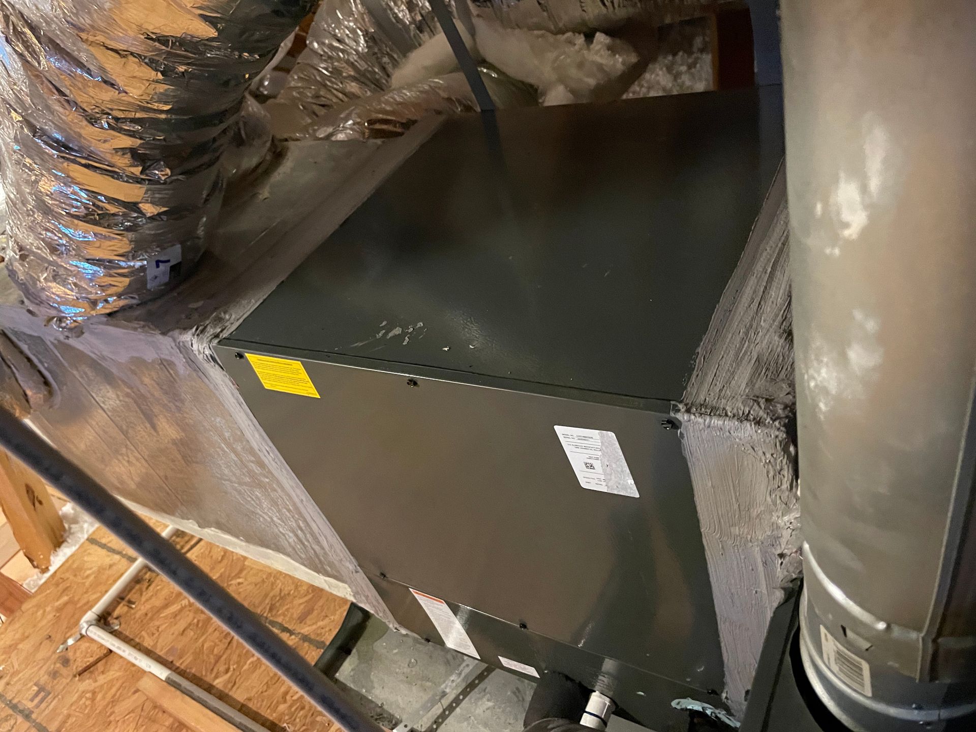 HVAC unit in an attic with insulated ductwork and a metal vent pipe.