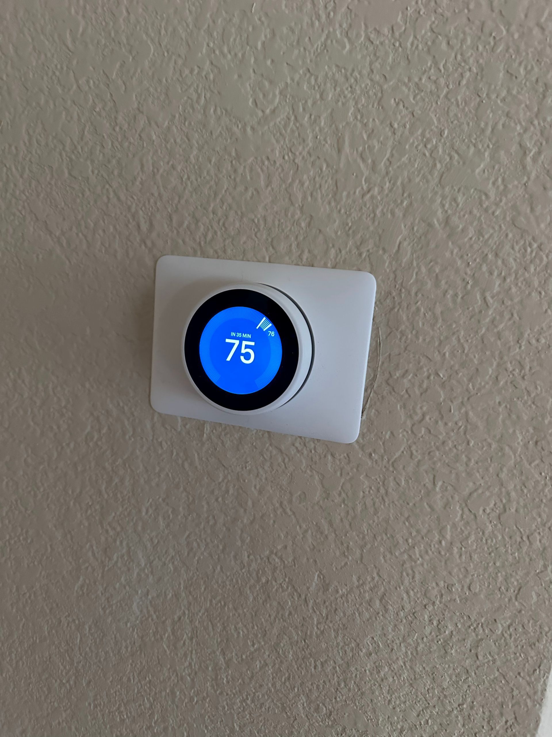 A Nest thermostat, showing 75 degrees, mounted on a beige wall.
