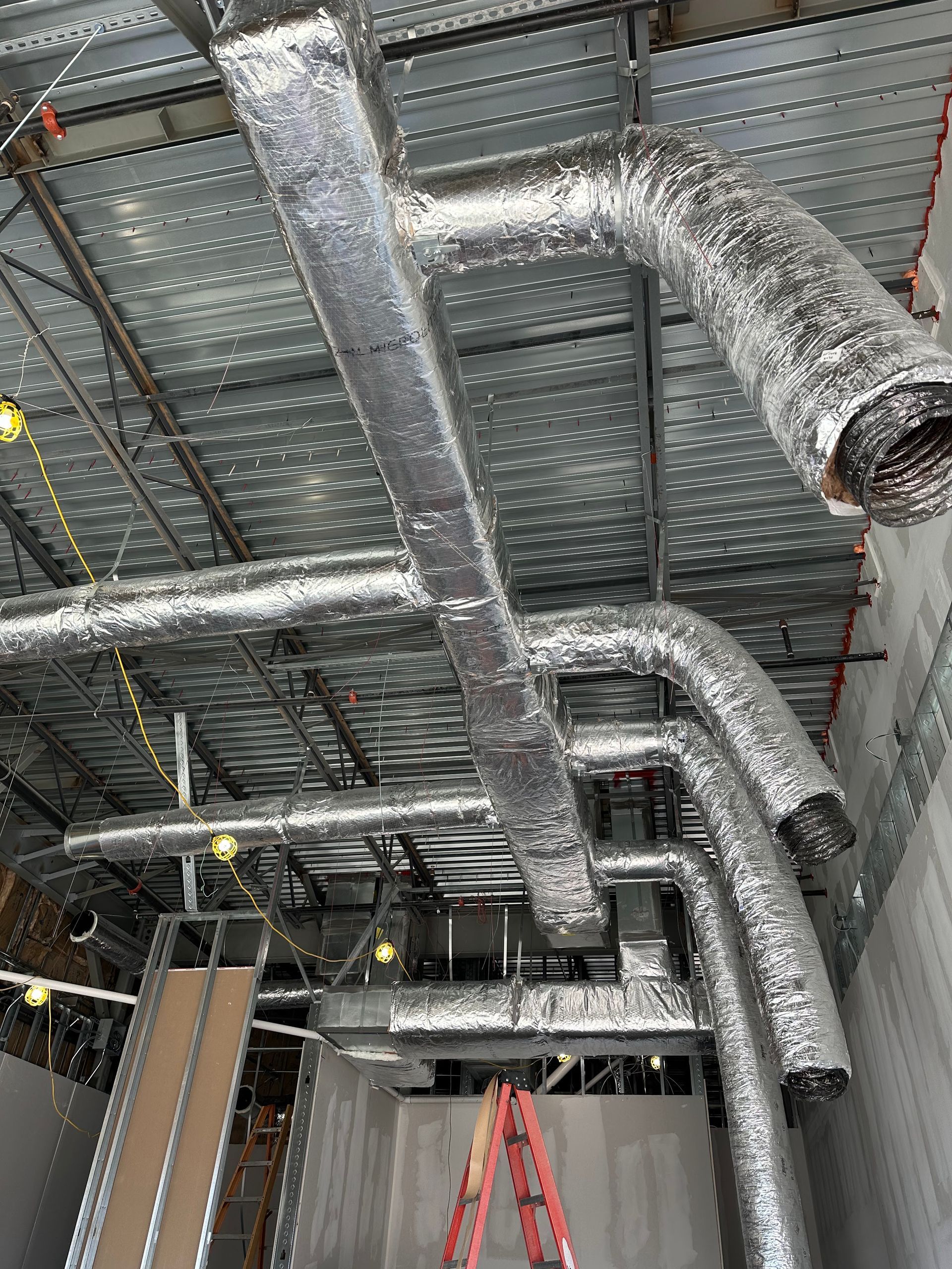 HVAC ductwork, silver insulated, runs across an unfinished ceiling, with a red ladder below.