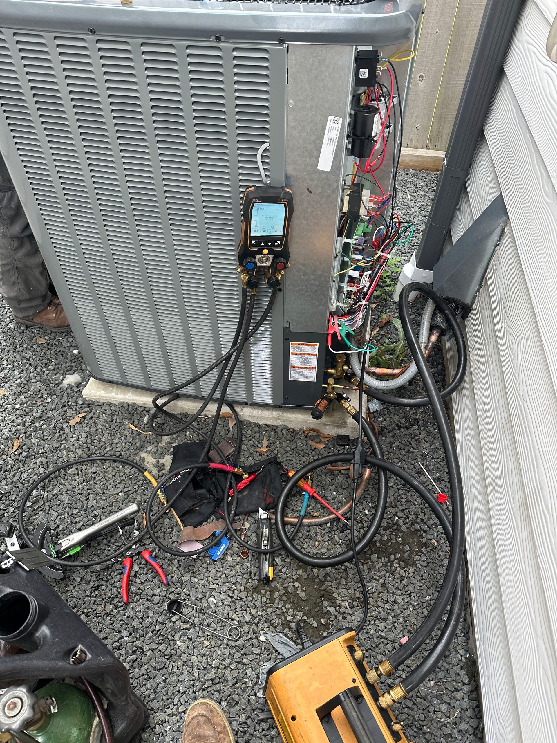 HVAC unit with gauges connected, set on gravel, being serviced outdoors.