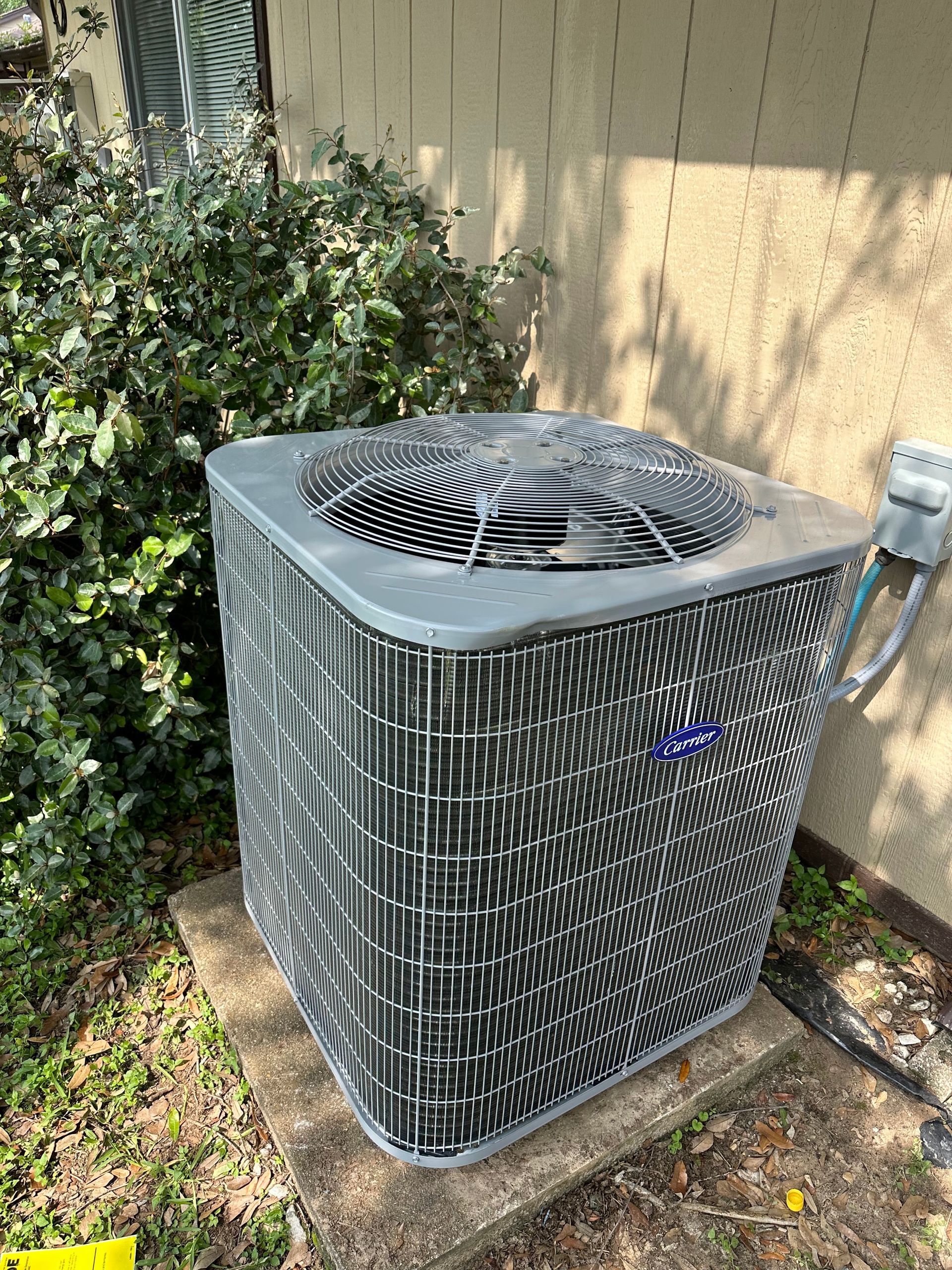Air conditioning unit outside a building, surrounded by greenery.