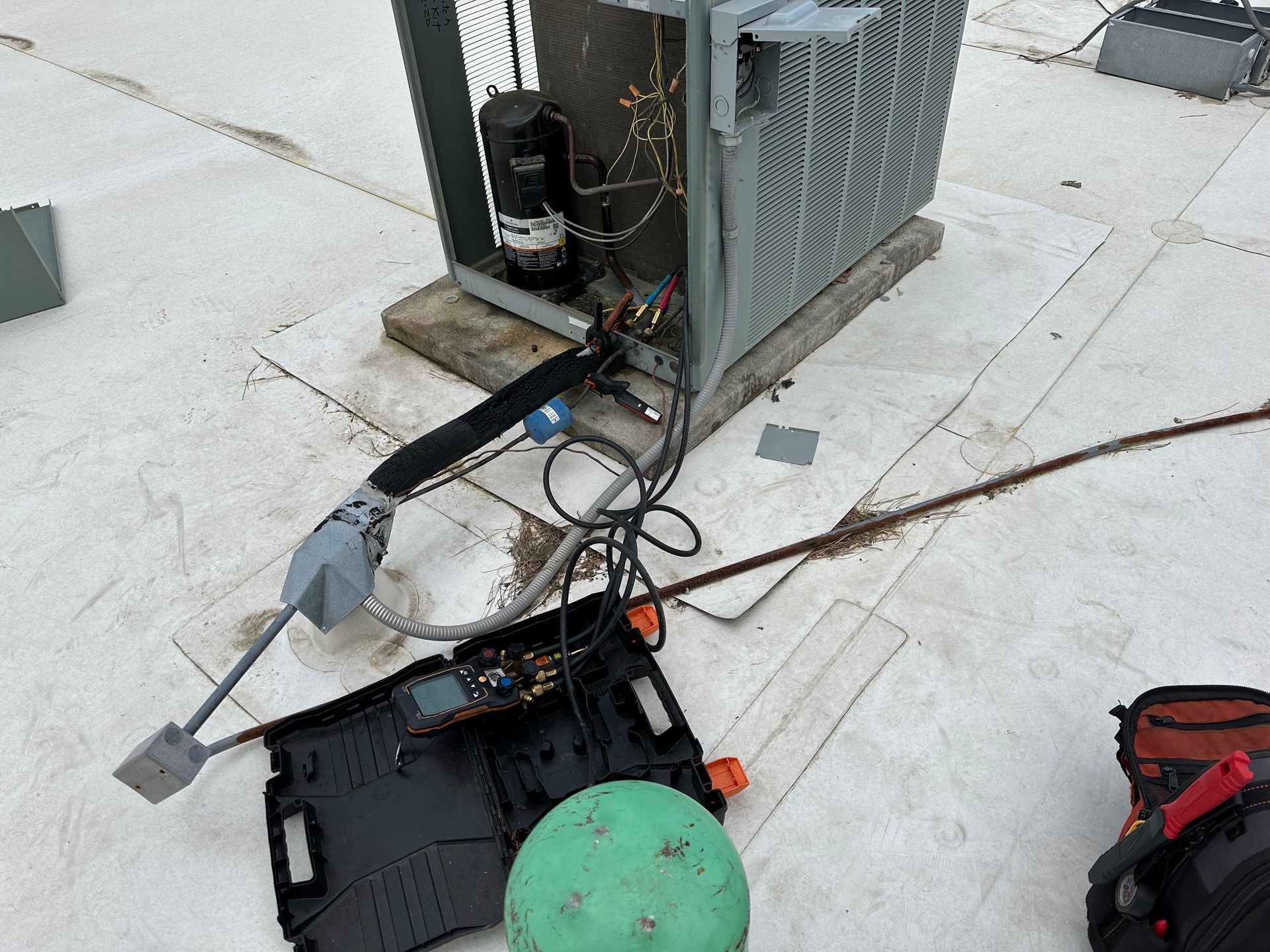 HVAC unit on a white rooftop being serviced. Tools, cables, and a black tray are present.