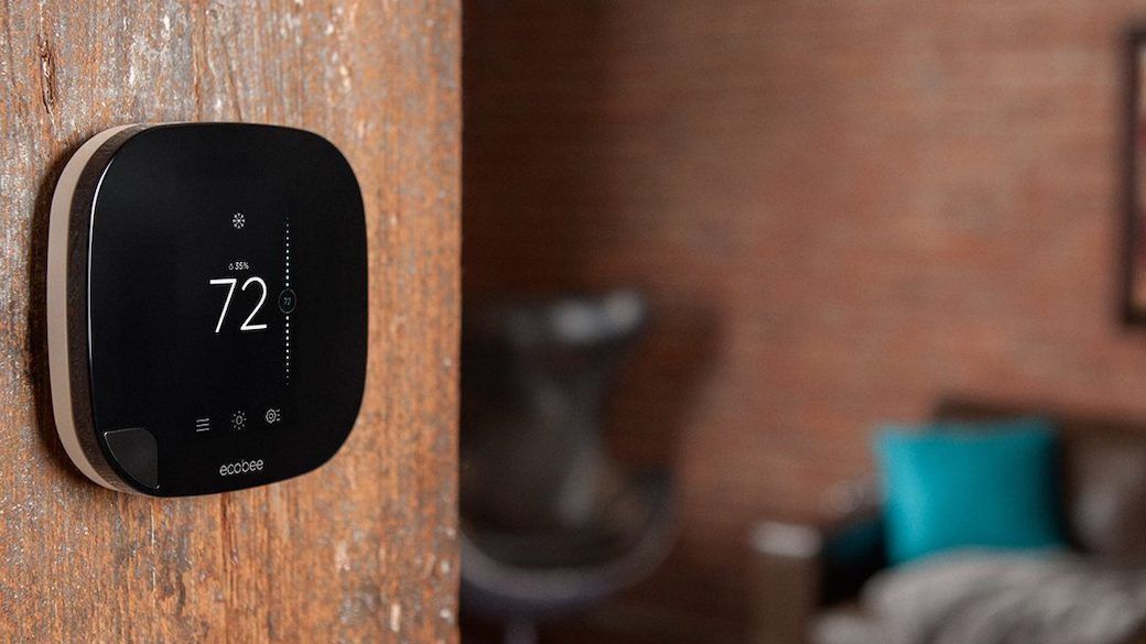 Smart thermostat on a wooden wall, displaying 72 degrees, with a brick wall and couch in the background.