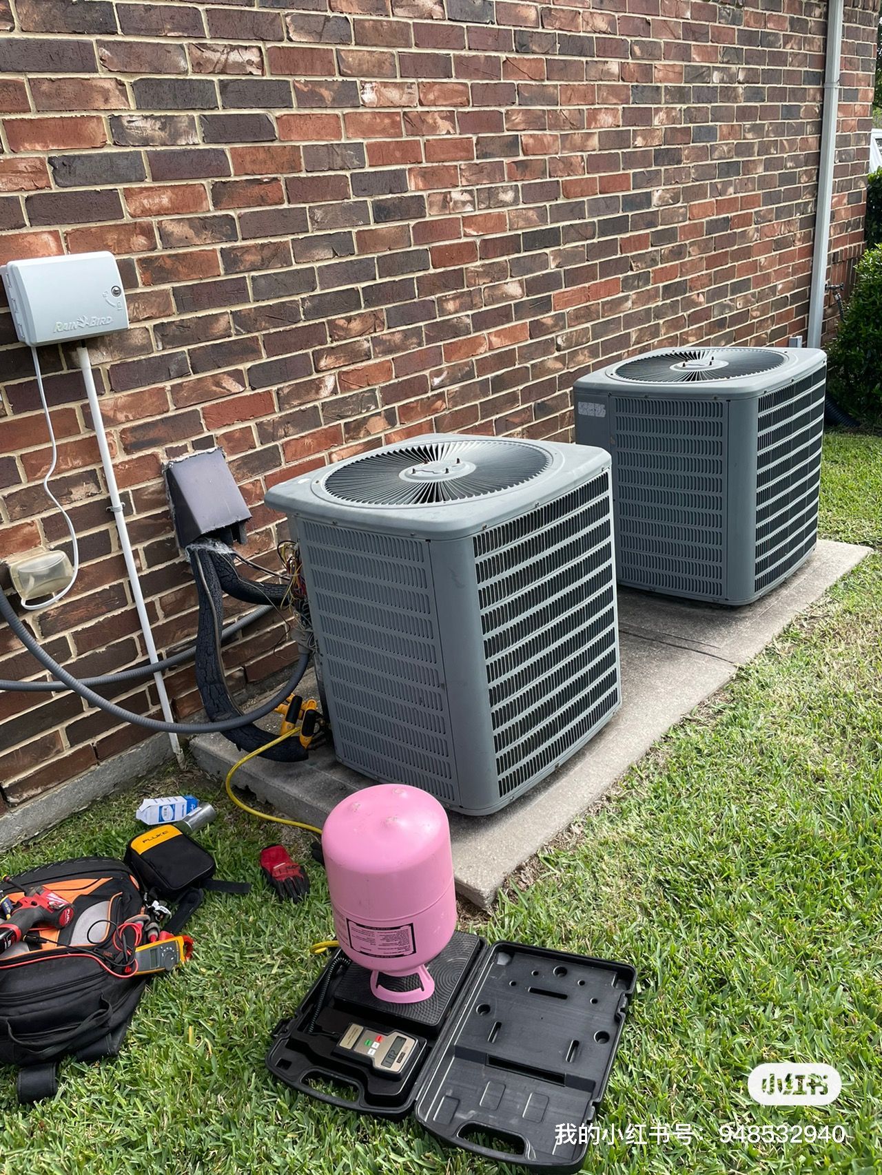 Two air conditioning units near a brick wall, with tools and components scattered on the grass.
