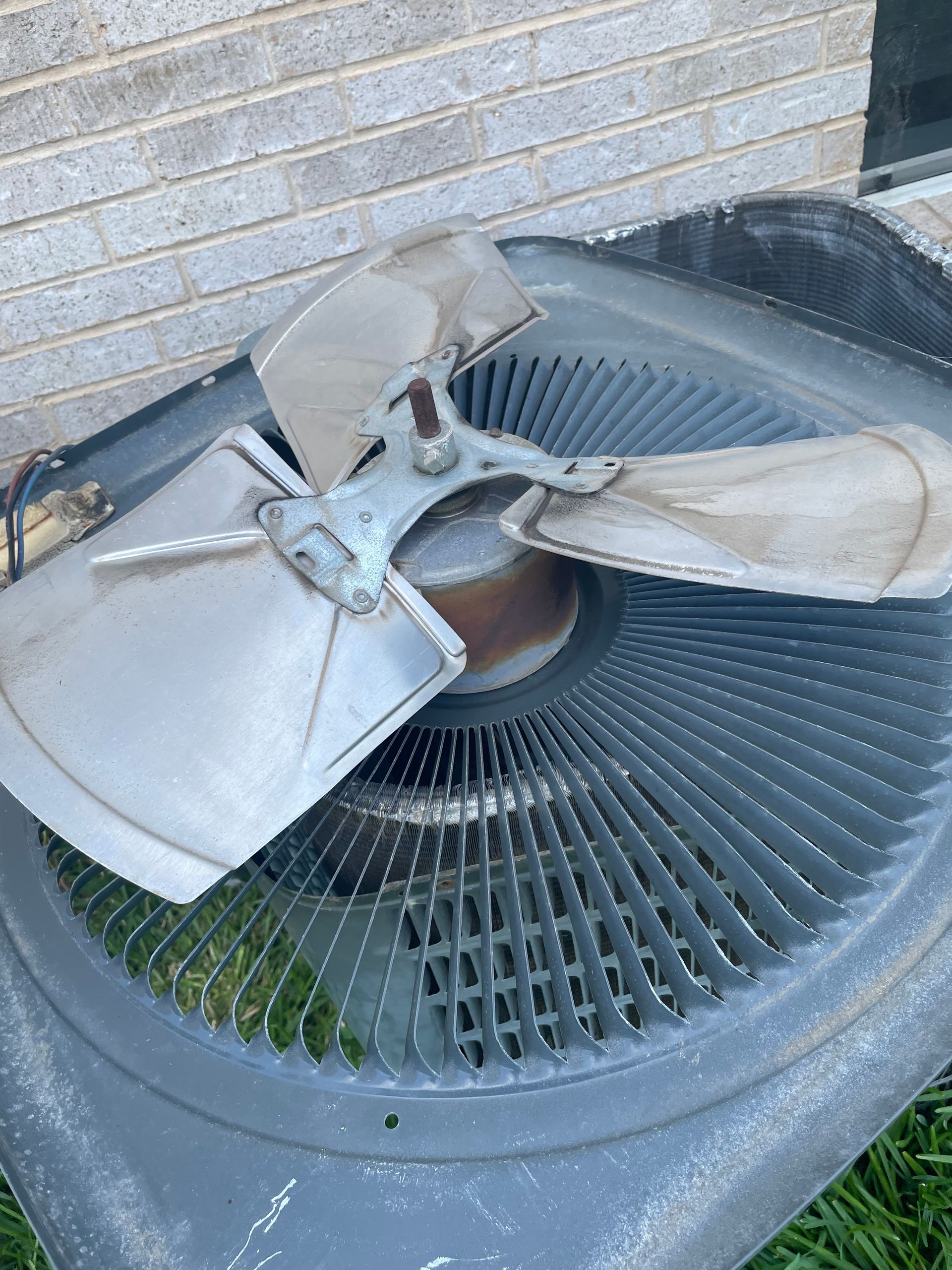 Air conditioning unit with damaged fan blades on a gray exterior.