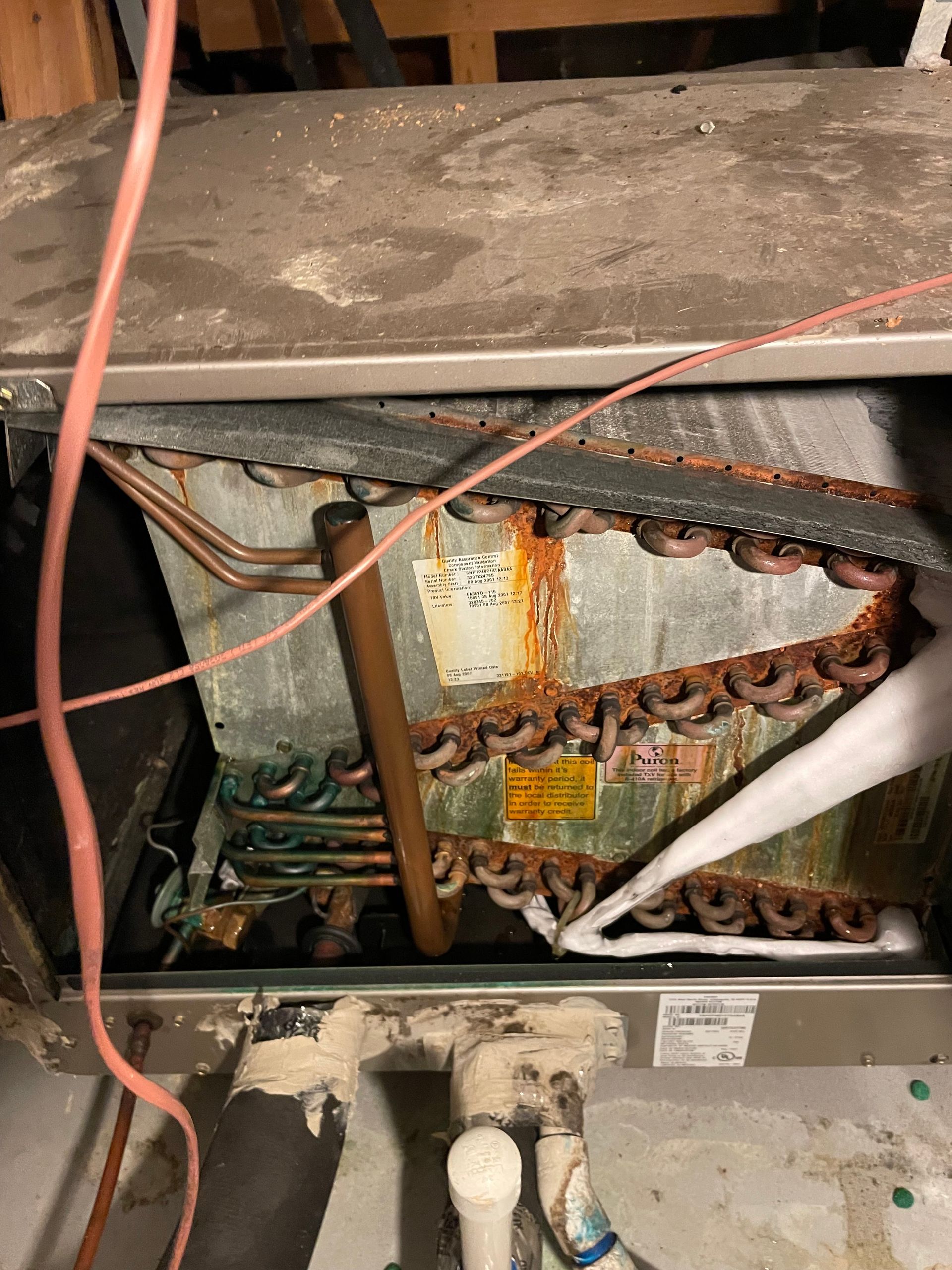 Rust-covered air conditioning unit with visible copper coils and insulated pipes.