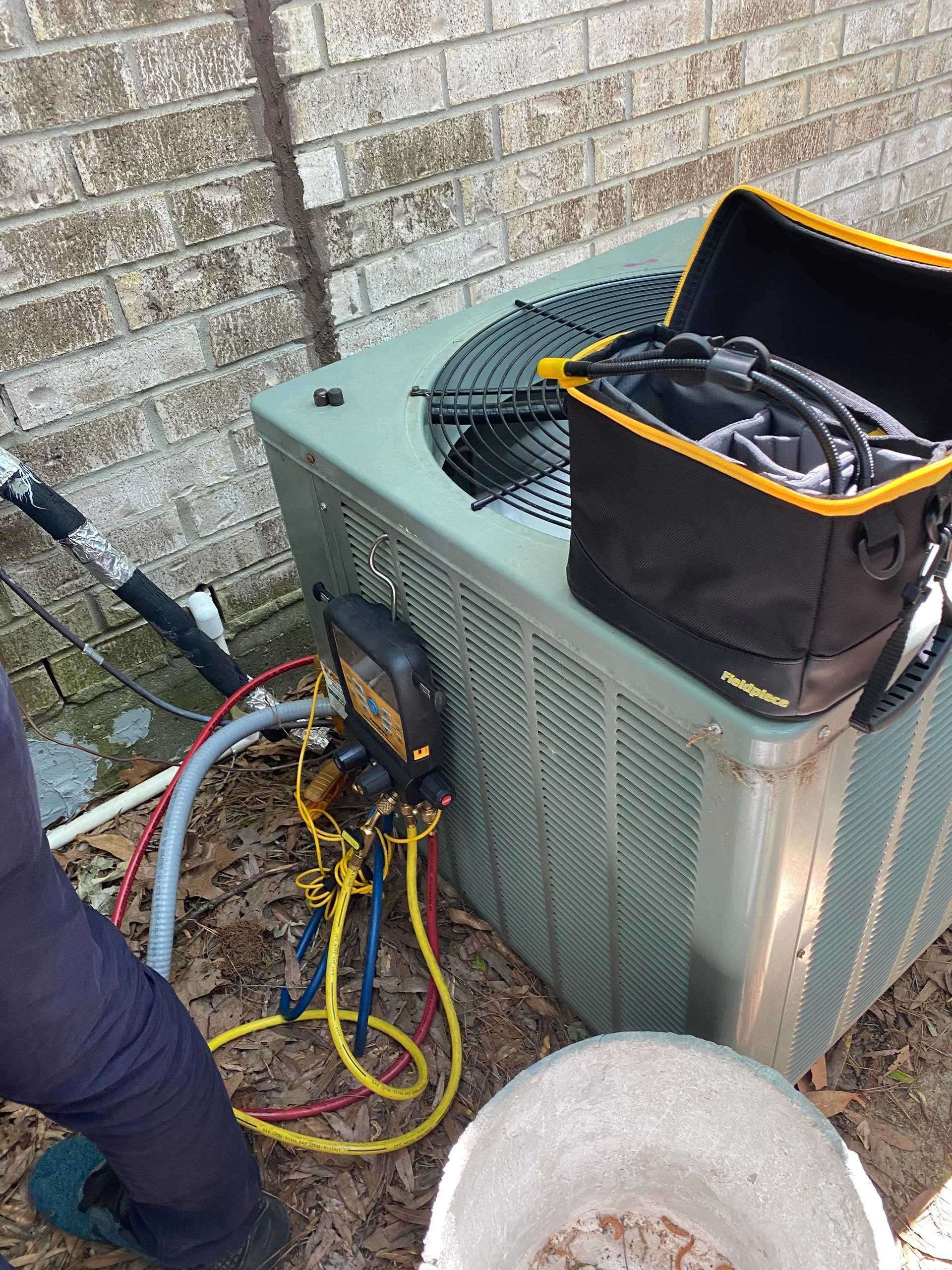 HVAC technician servicing an outdoor air conditioning unit with gauges and tools.