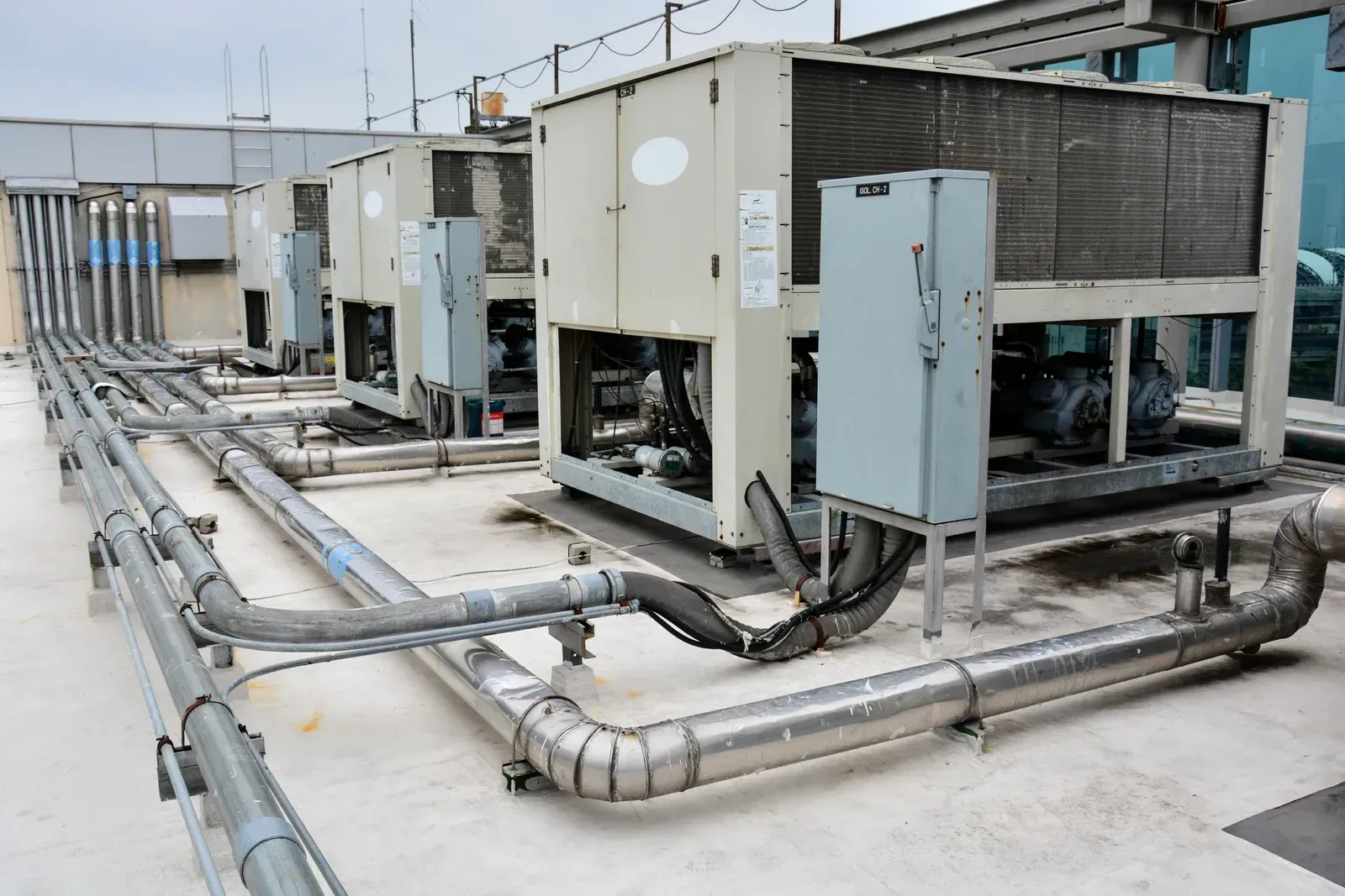 HVAC units on a rooftop with silver pipes, cooling towers, and control boxes.