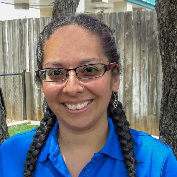 A woman wearing glasses and braids is smiling in front of a wooden fence.