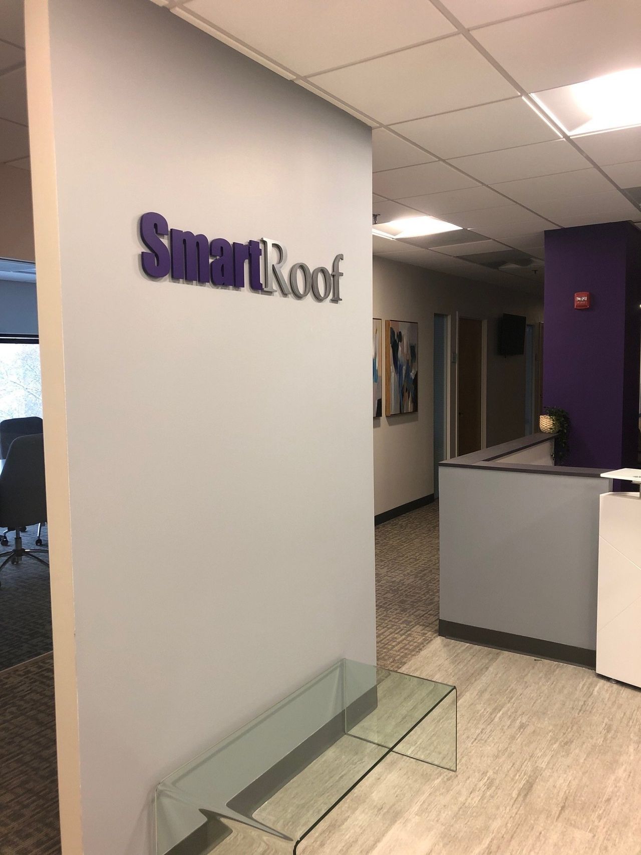 Office lobby with SmartRoof sign, reception desk, and glass bench in a hallway corner