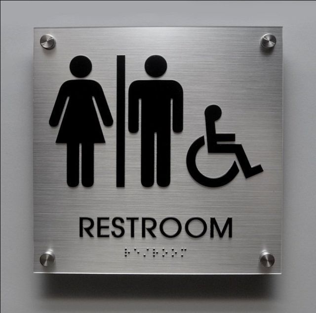 Metal restroom sign with male, female, and wheelchair accessibility symbols on a brushed silver plaque