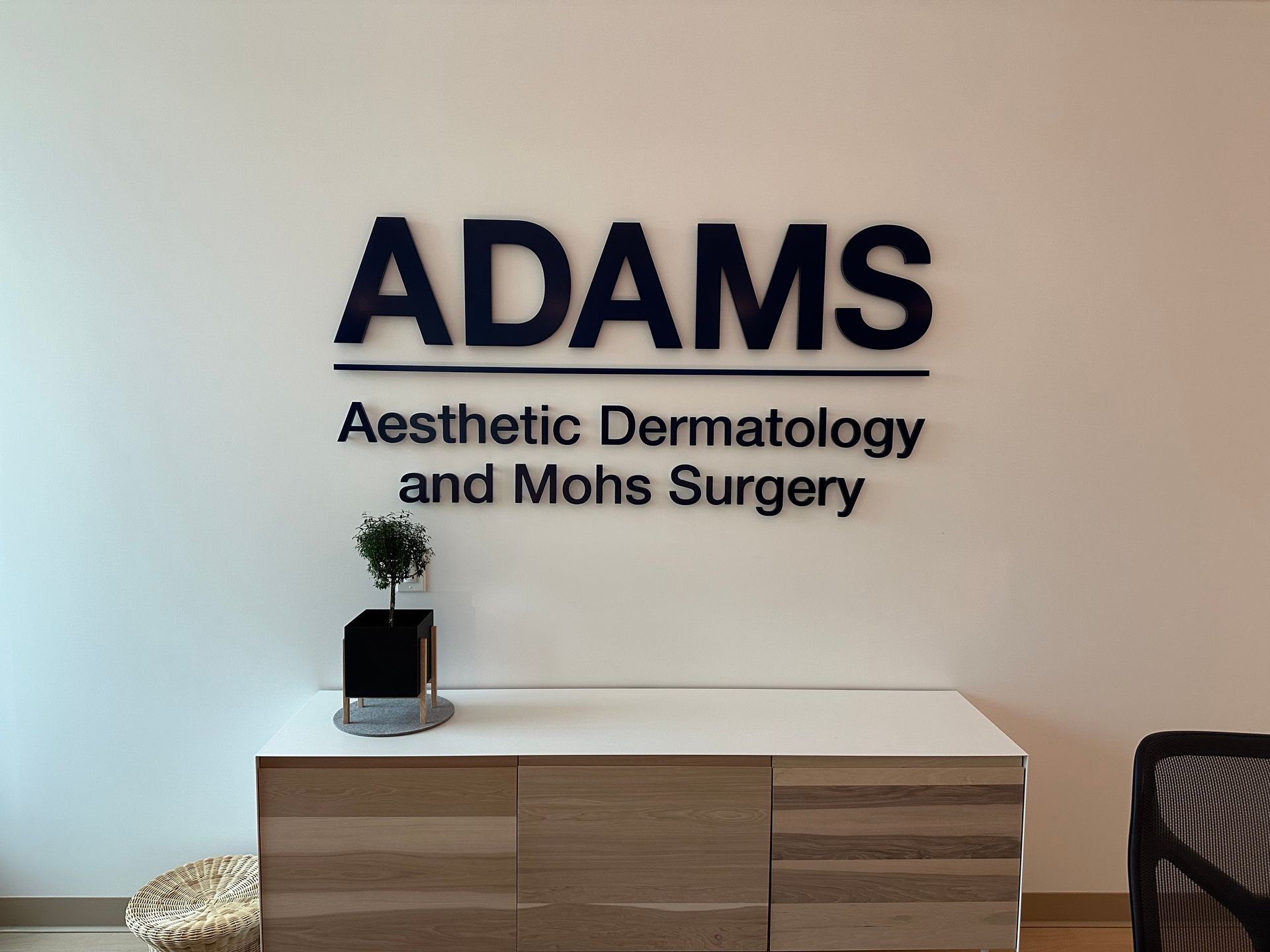 ADAMS Aesthetic Dermatology and Mohs Surgery sign above a lobby cabinet with plant and decor