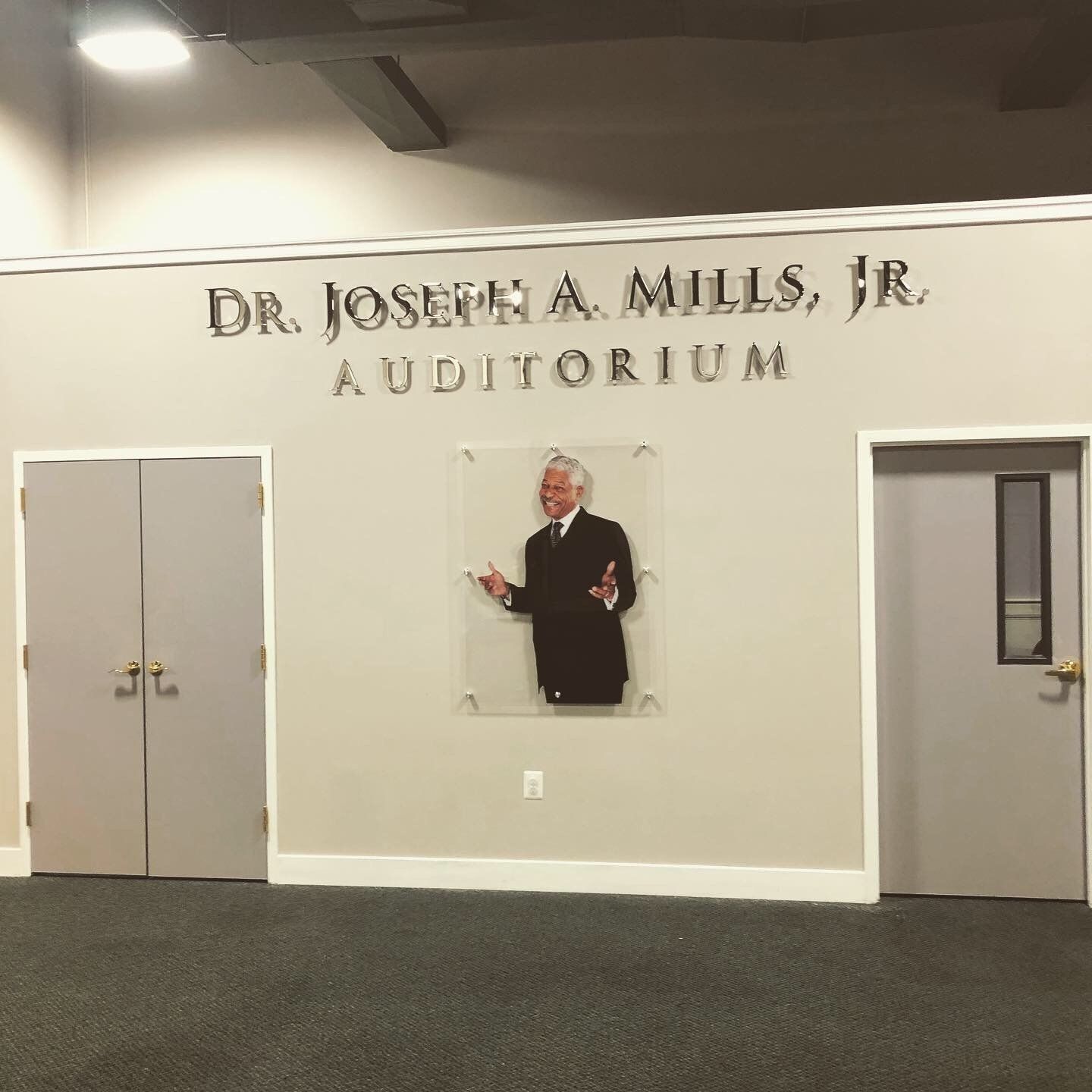 Auditorium wall with “Dr. Joseph A. Mills, Jr.” sign, doors, and a cutout of a man in a suit