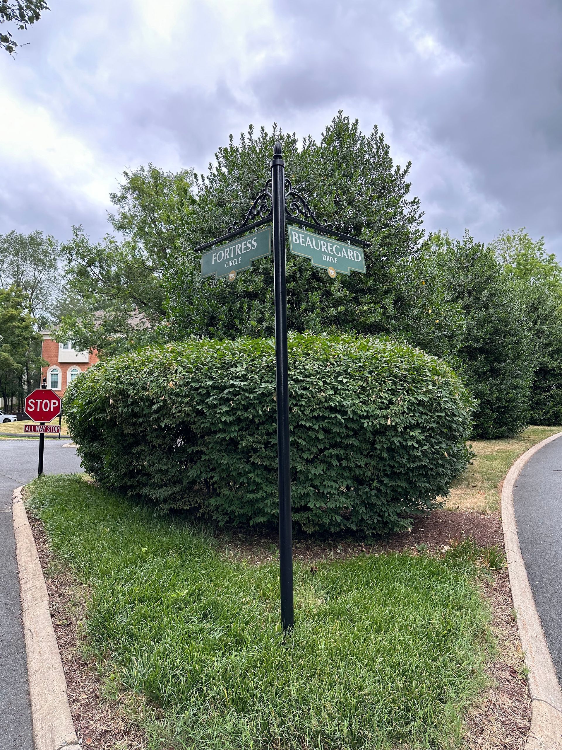 Street signs at a leafy roundabout with a stop sign in the background