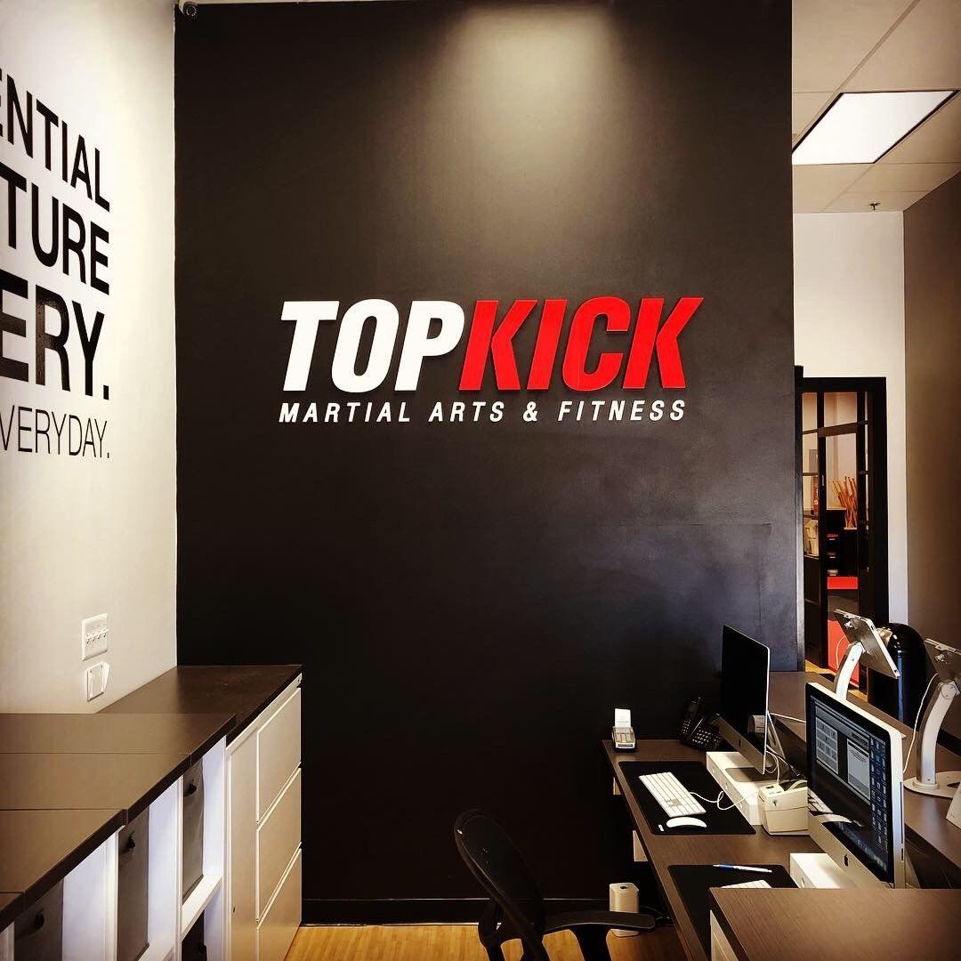 Reception area with black wall sign reading “TOPKICK Martial Arts & Fitness”