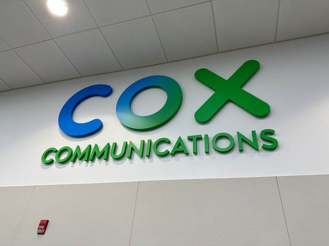 Cox Communications logo in blue and green on a white wall inside a building