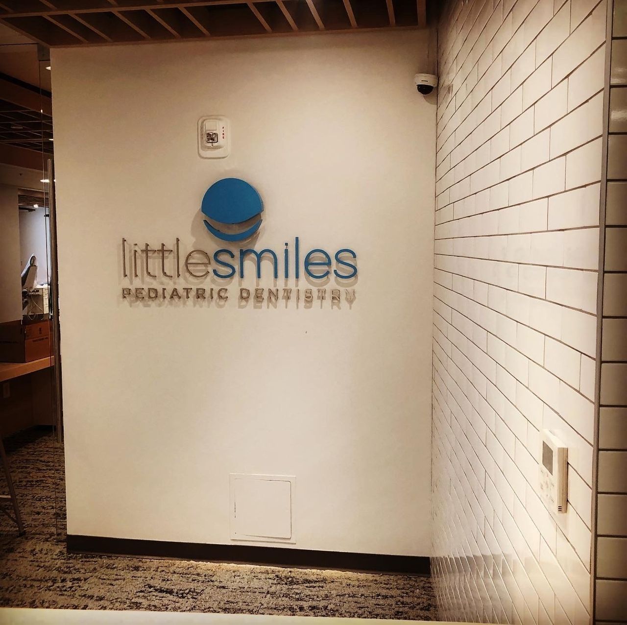 Wall sign for Little Smiles Pediatric Dentistry on a white hallway wall.