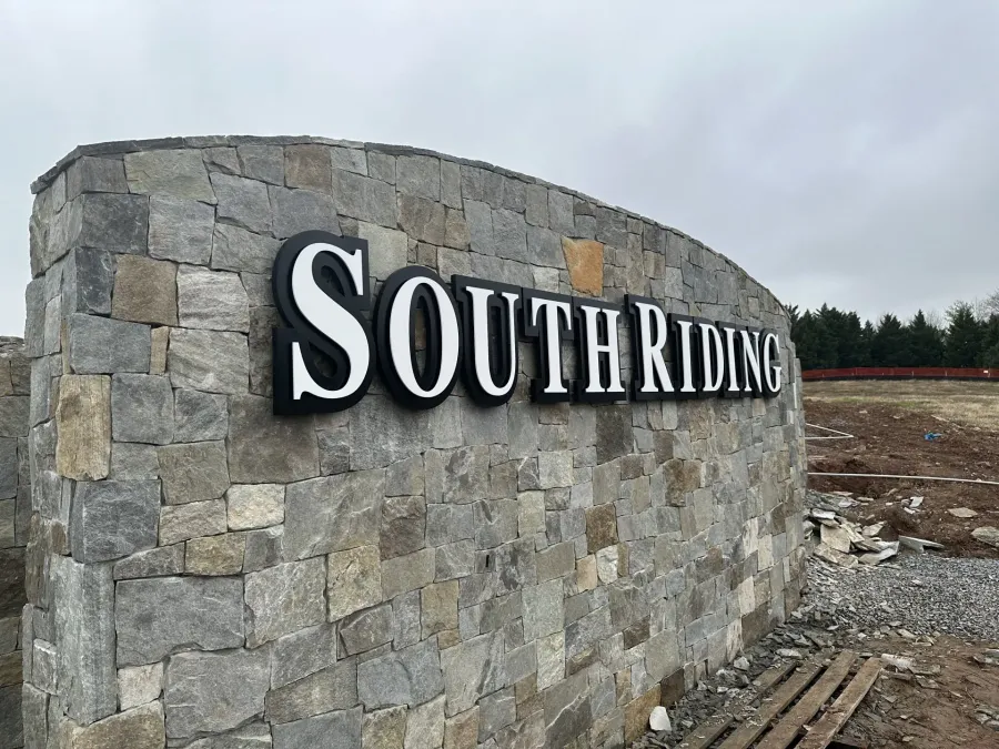A stone community entrance sign reading "South Riding" in bold, black-and-white lettering under a cloudy sky.
