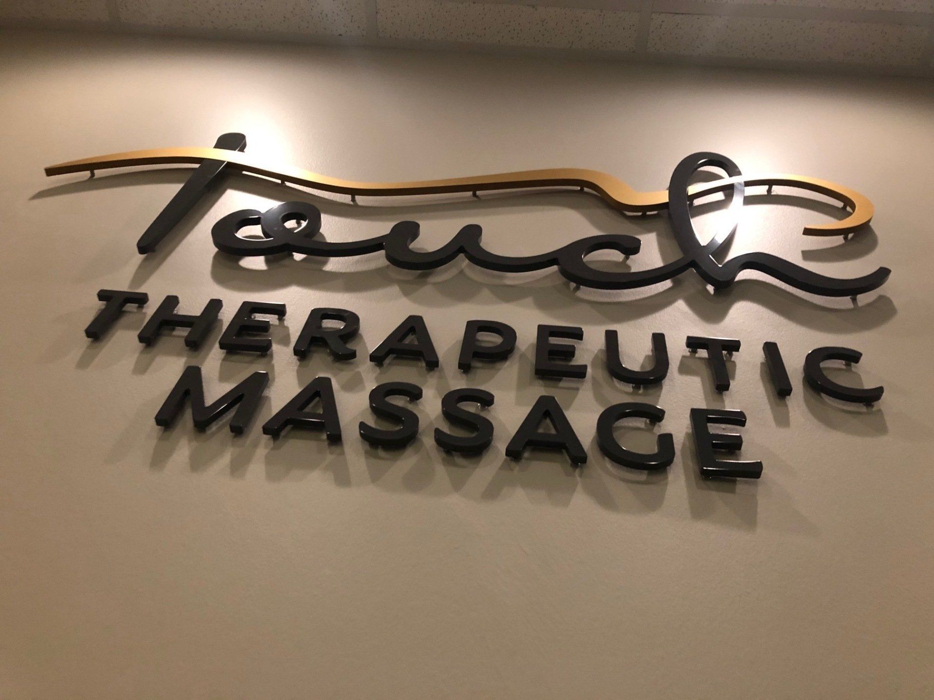 Therapeutic massage wall sign in black letters with gold script accents