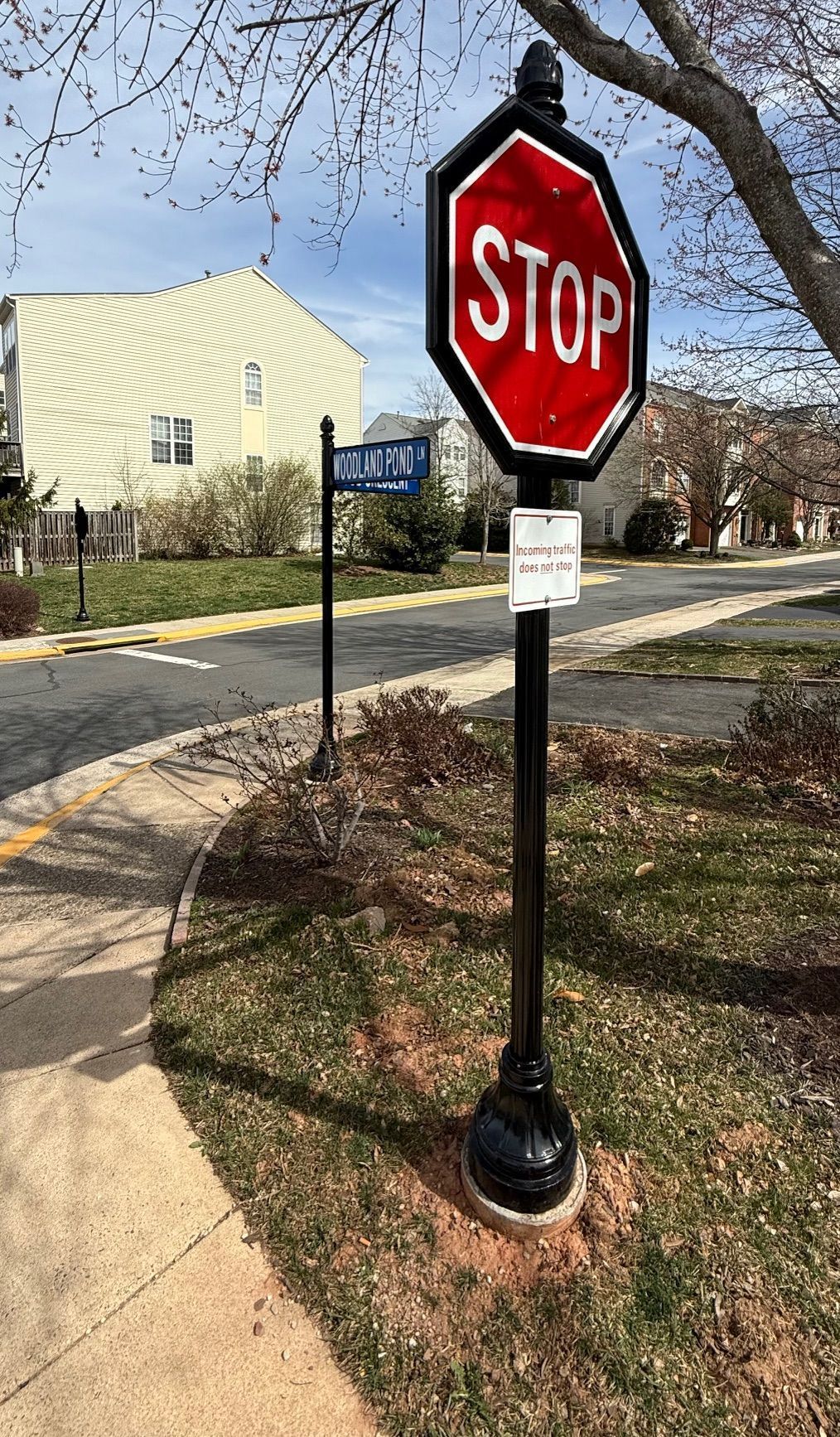 Red stop sign on a pole beside a sidewalk near a building and trees.
