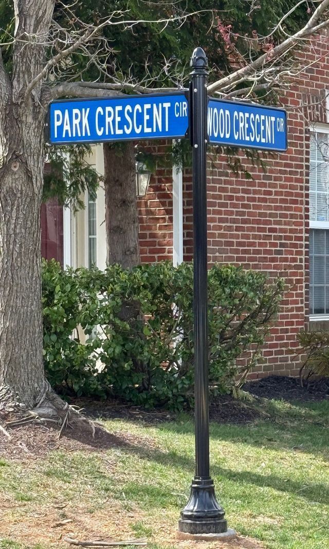 Blue street signs reading “PARK CRESCENT” and “N STREET” on a black post by a brick building.